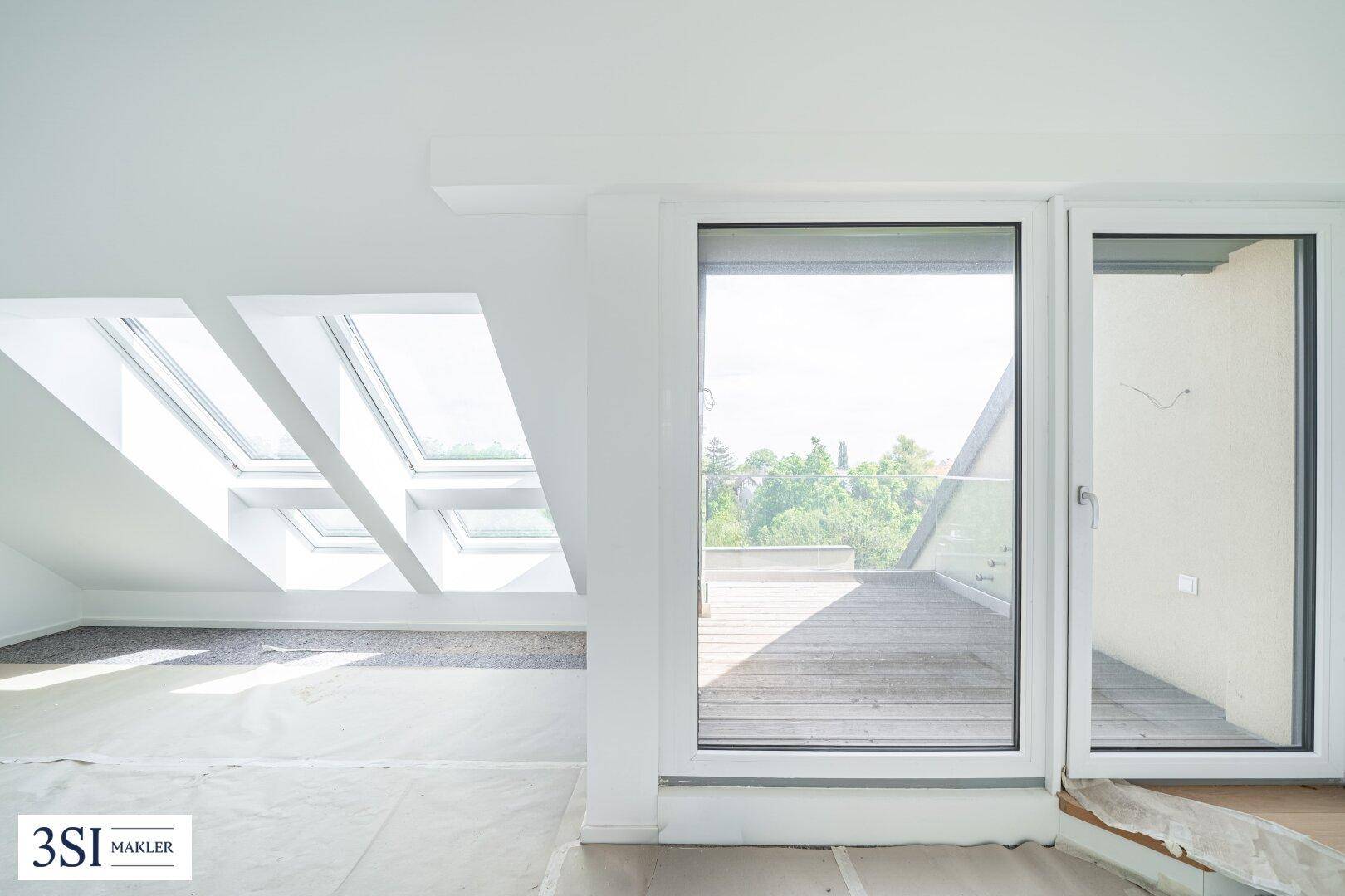 Dachgeschossraum mit Dachfenstern und Zugang zu einer sonnigen Terrasse.