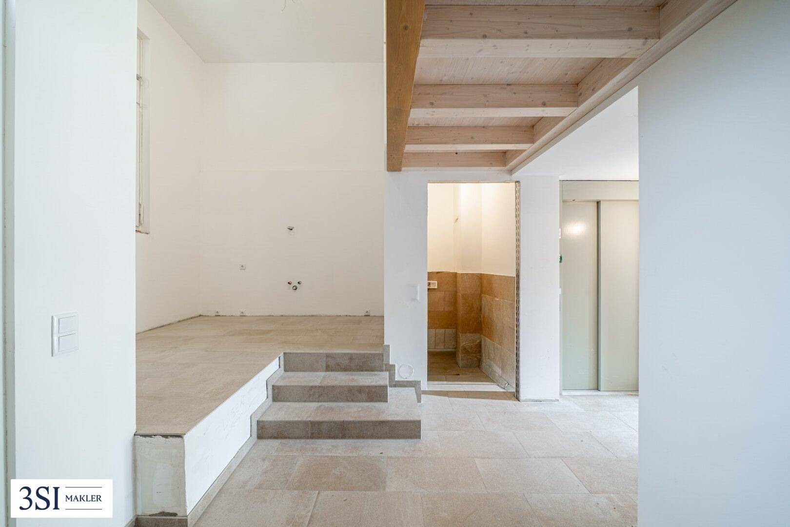 Unfertiger Innenraum mit Steinfliesen, Treppe und sichtbaren Installationen im Rohbauzustand.