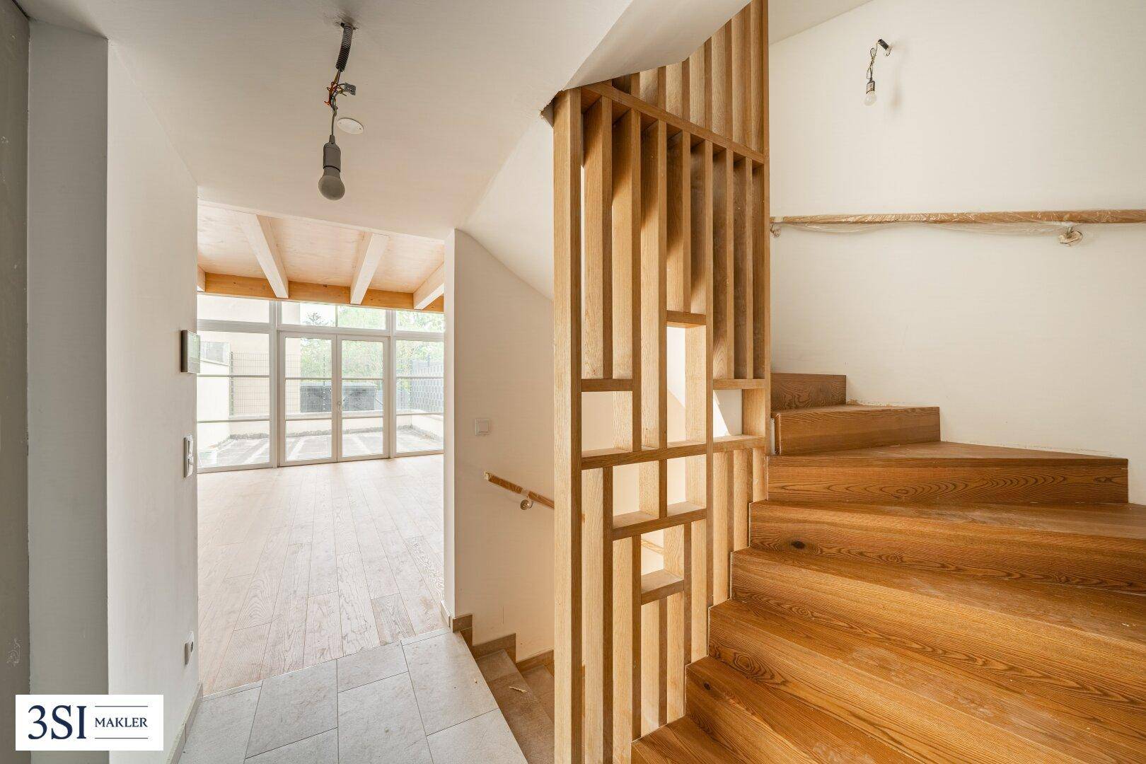 Heller Flur mit Holztreppe, Holzboden und Blick in den Wohnbereich des Neubaus.