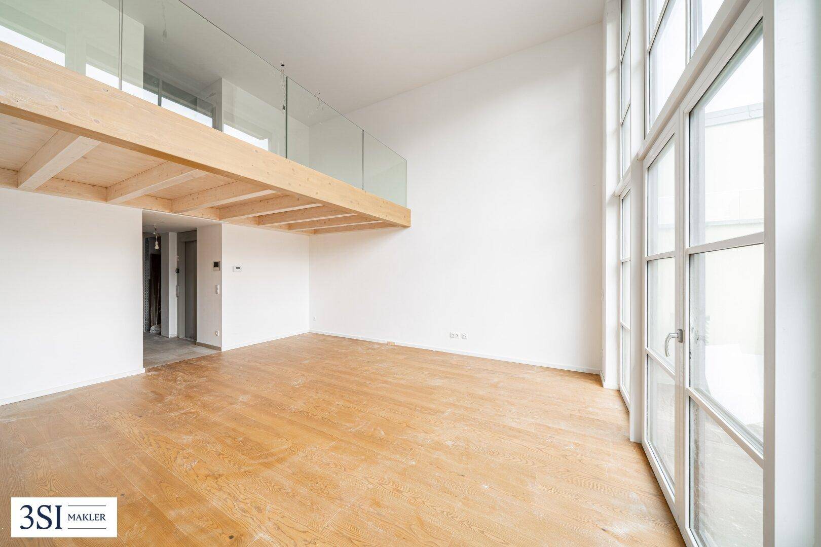 Hoher, unmöblierter Raum mit Holzbalkendecke, Galerie und großen Fenstern.