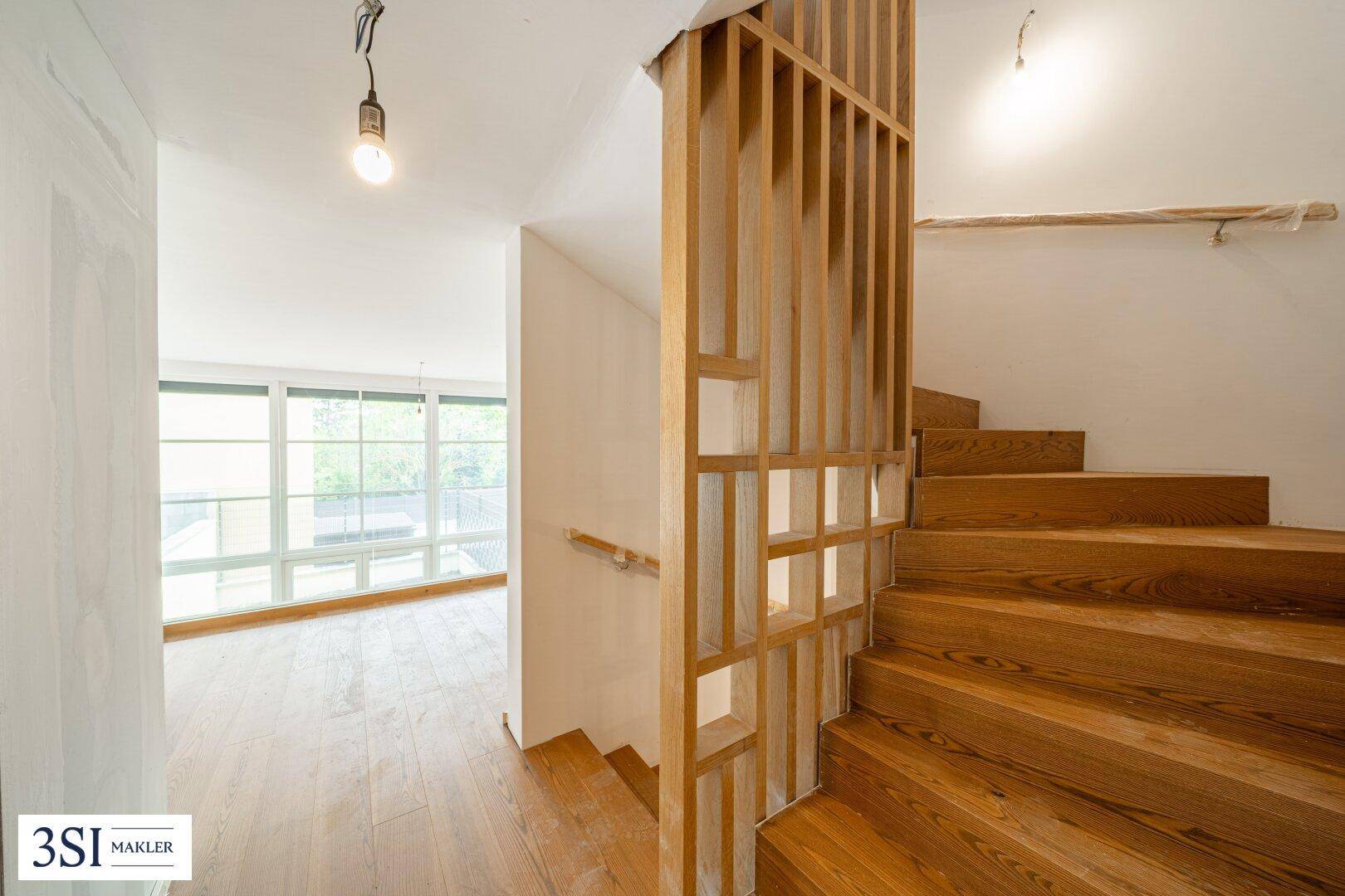 Heller Flur mit Holztreppe, Holzboden und Blick in den Wohnbereich des Neubaus.