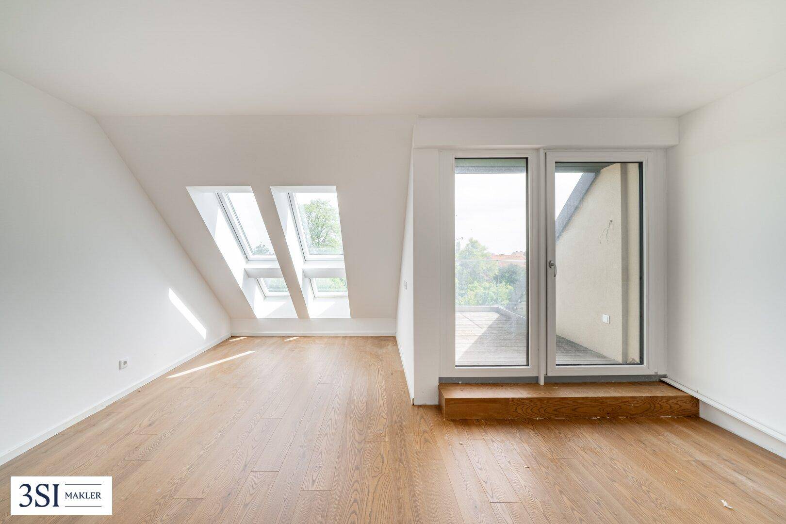 Helles Dachzimmer mit Holzboden, Dachfenstern und Zugang zu einem kleinen Balkon.