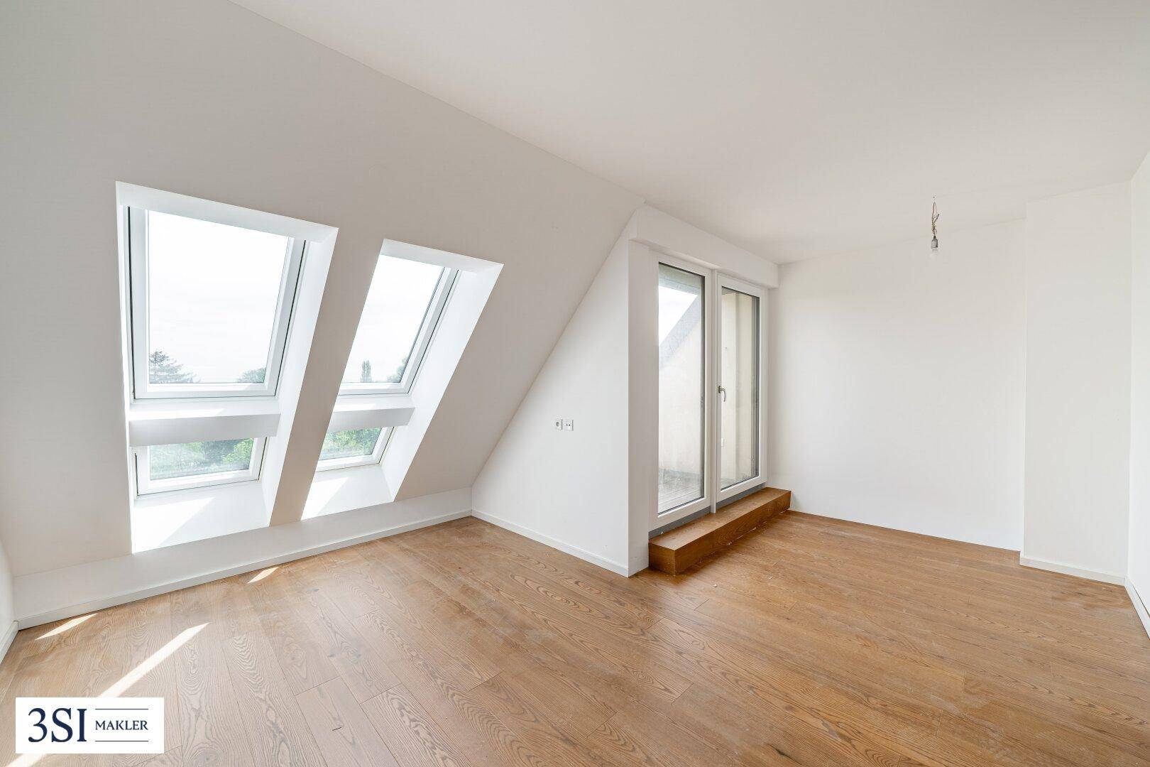 Heller Dachgeschossraum mit Holzboden, großen Dachfenstern und Zugang zu einem französischen Balkon.