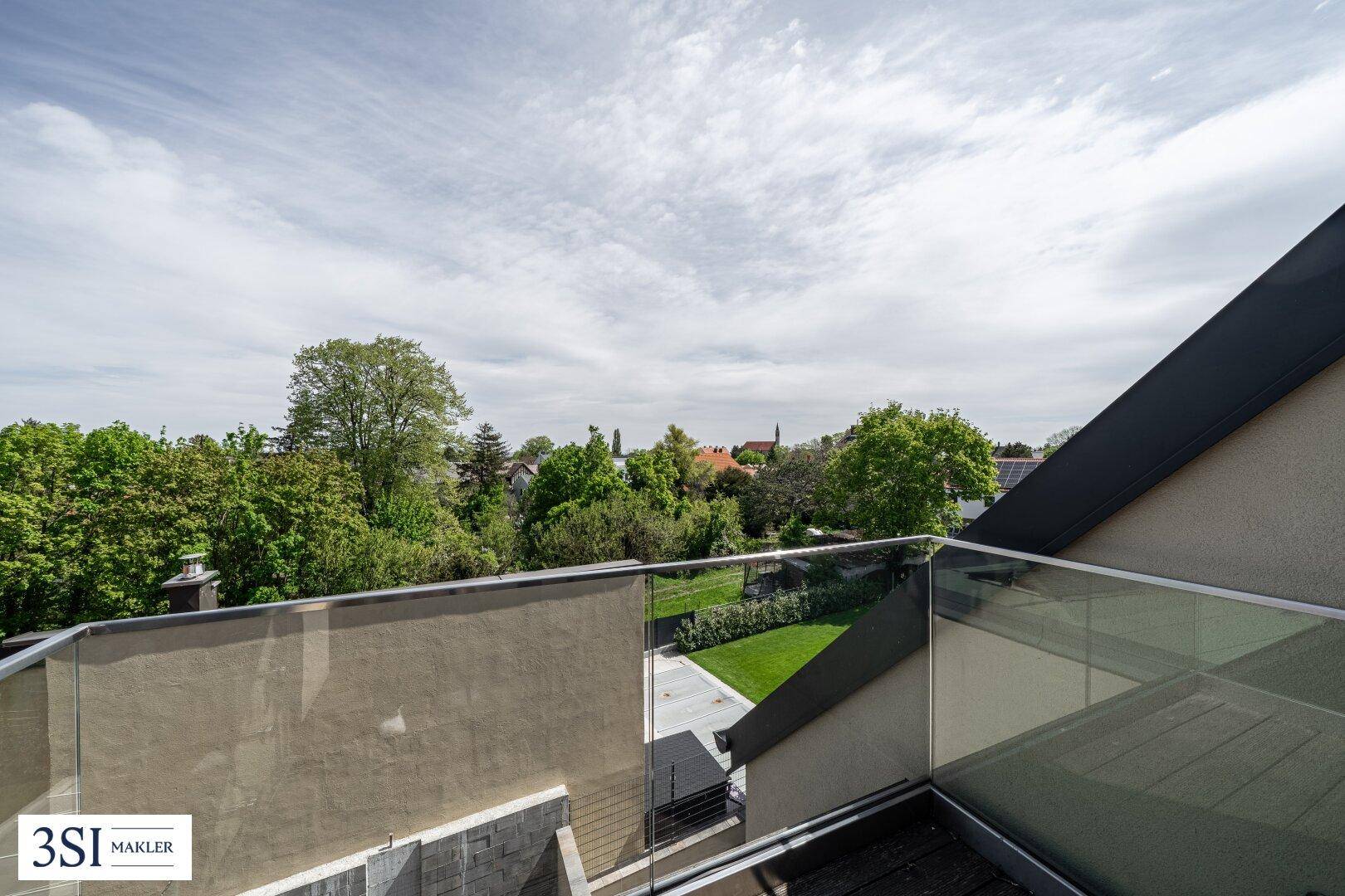 Moderne Dachterrasse mit Glasgeländer bietet einen weiten Blick über grüne Bäume und die Umgebung.