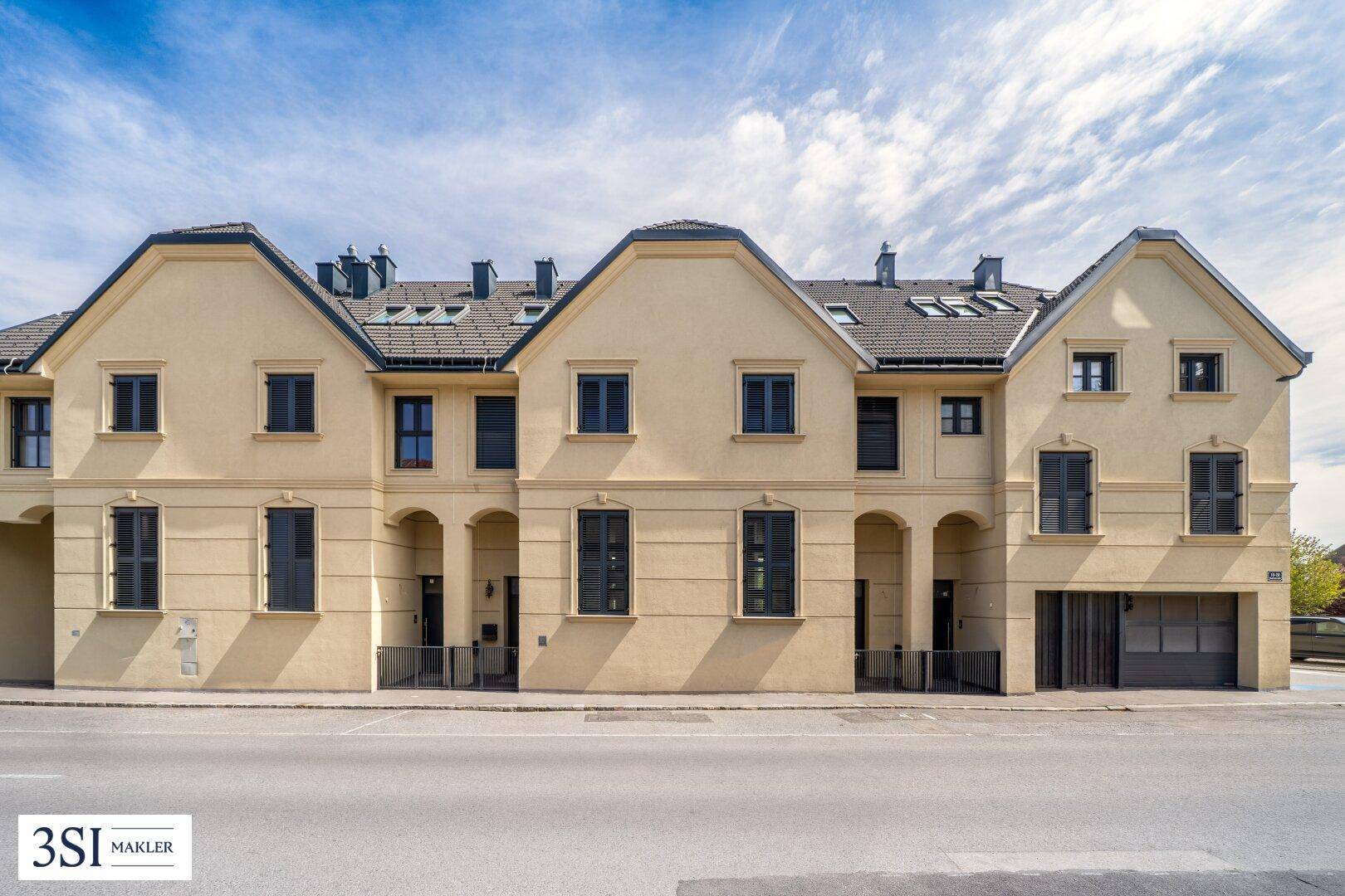 Moderne Reihenhäuser mit klassischer Fassade, dunklen Fenstern und Satteldächern an der Straße.