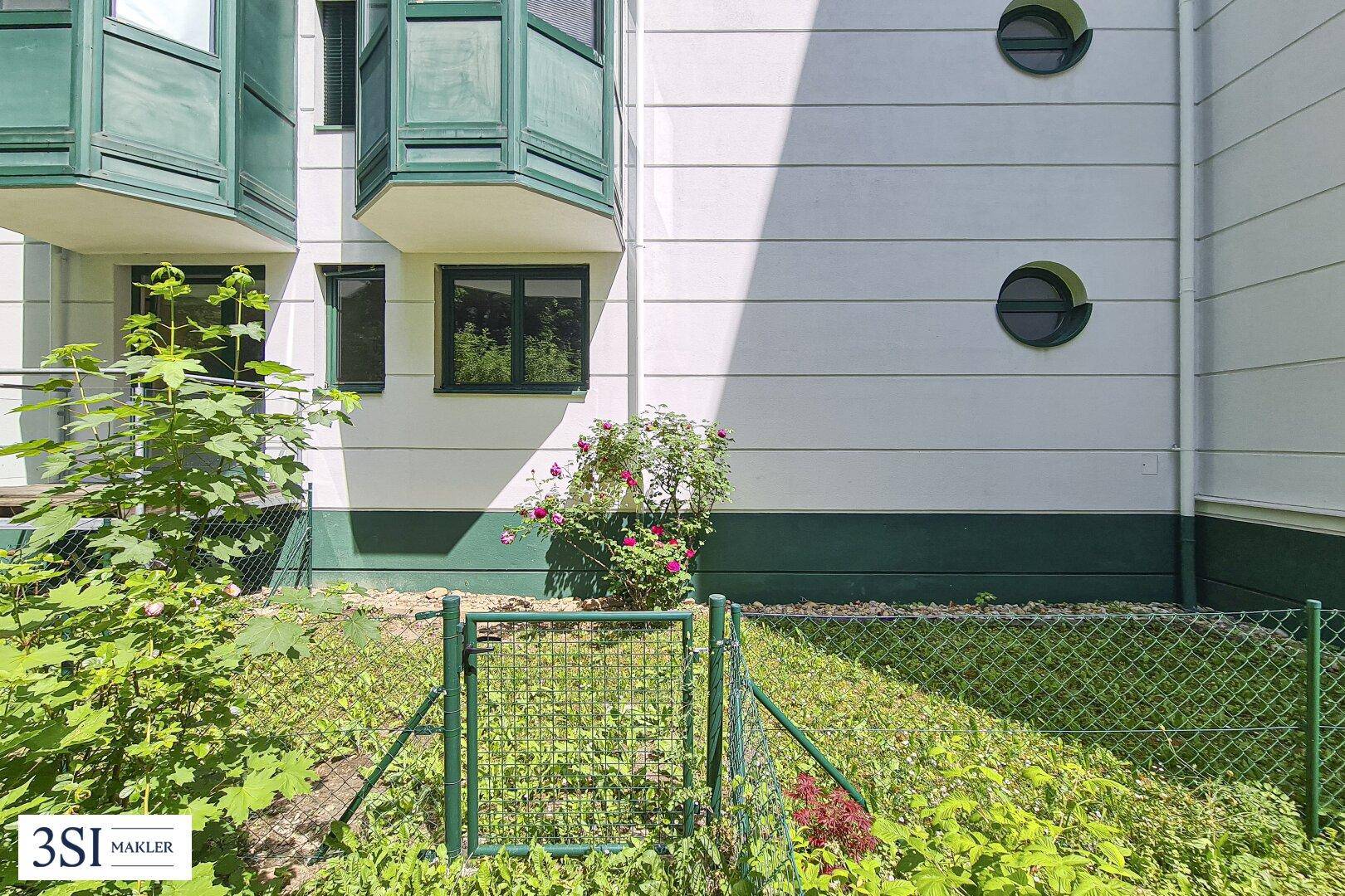 Gartenansicht mit blühenden Rosen und runden Fenstern an der modernen Gebäudefassade.