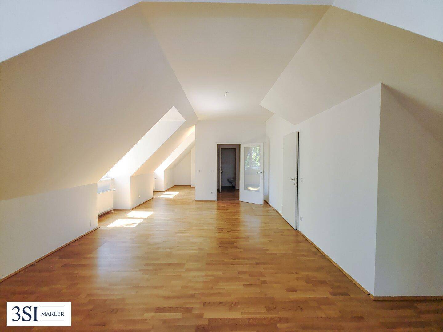 Großer, heller Raum im Dachgeschoss mit Holzboden, schrägen Decken und mehreren Dachfenstern.