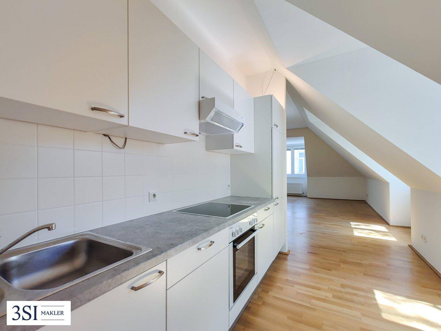 Moderne Einbauküche in Weiß mit grauer Arbeitsplatte und Dachschrägen in einer hellen Wohnung.