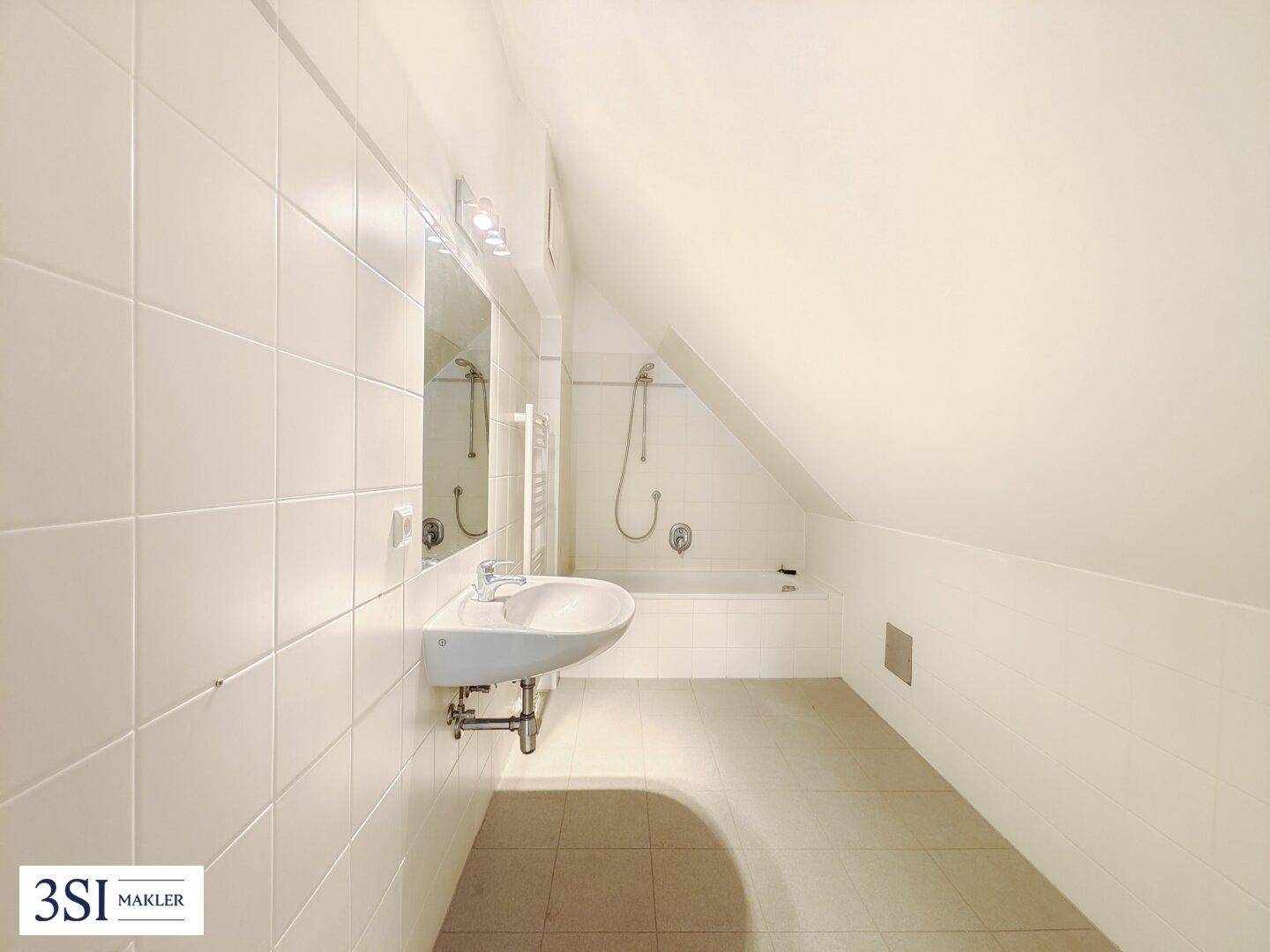 Helles Badezimmer mit weißen Fliesen, Waschbecken und Badewanne unter einer Dachschräge.