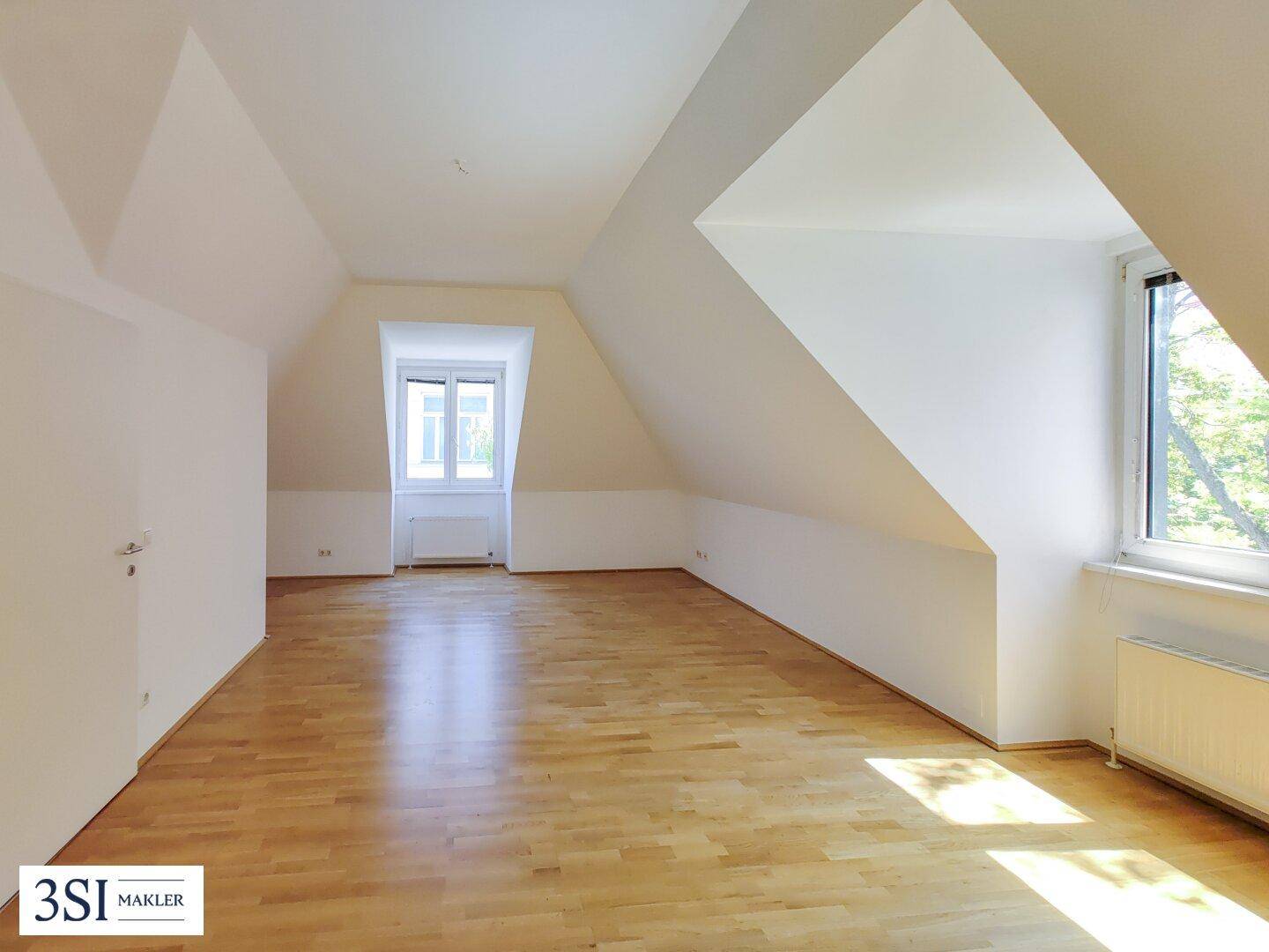 Geräumiger, leerer Wohnbereich im Dachgeschoss mit Holzboden und viel Tageslicht.
