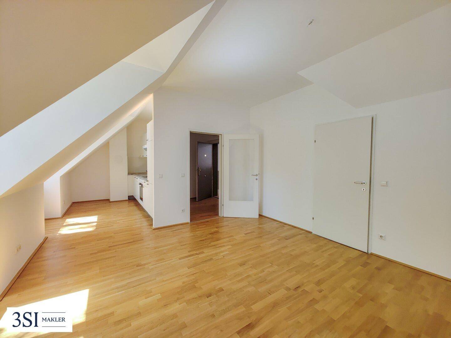 Geräumiger Wohnbereich mit Holzboden und Blick auf die offene Küche in einer Dachgeschosswohnung.