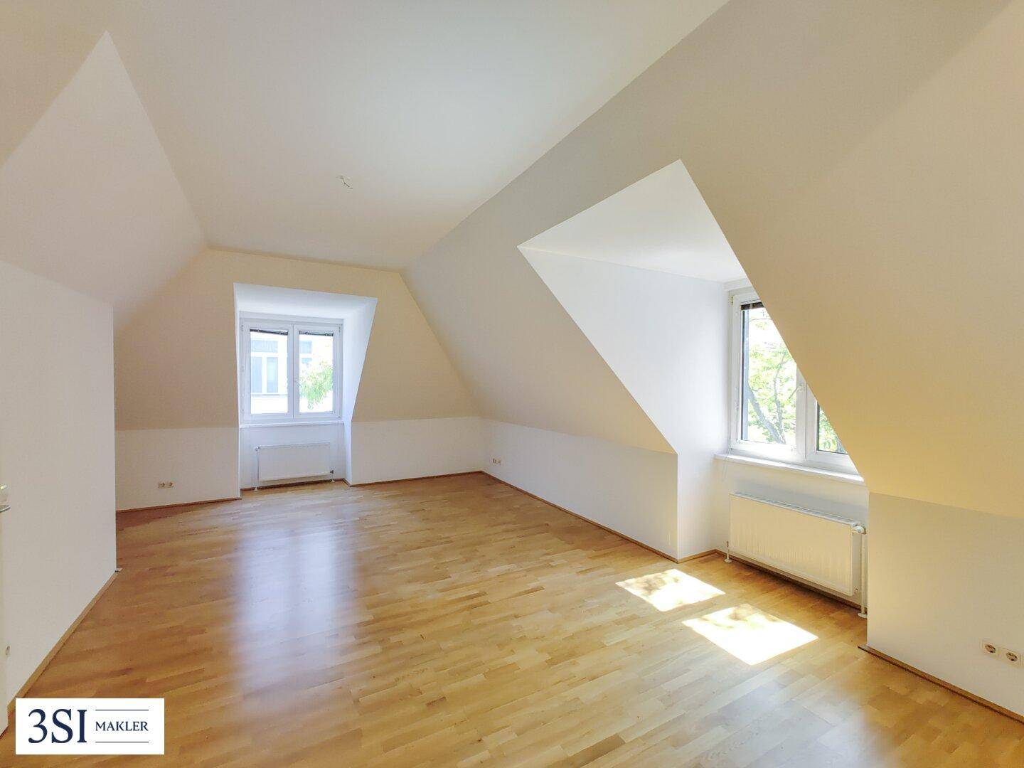 Heller, leerer Wohnraum in einer Dachgeschosswohnung mit Holzboden und schrägen Wänden.