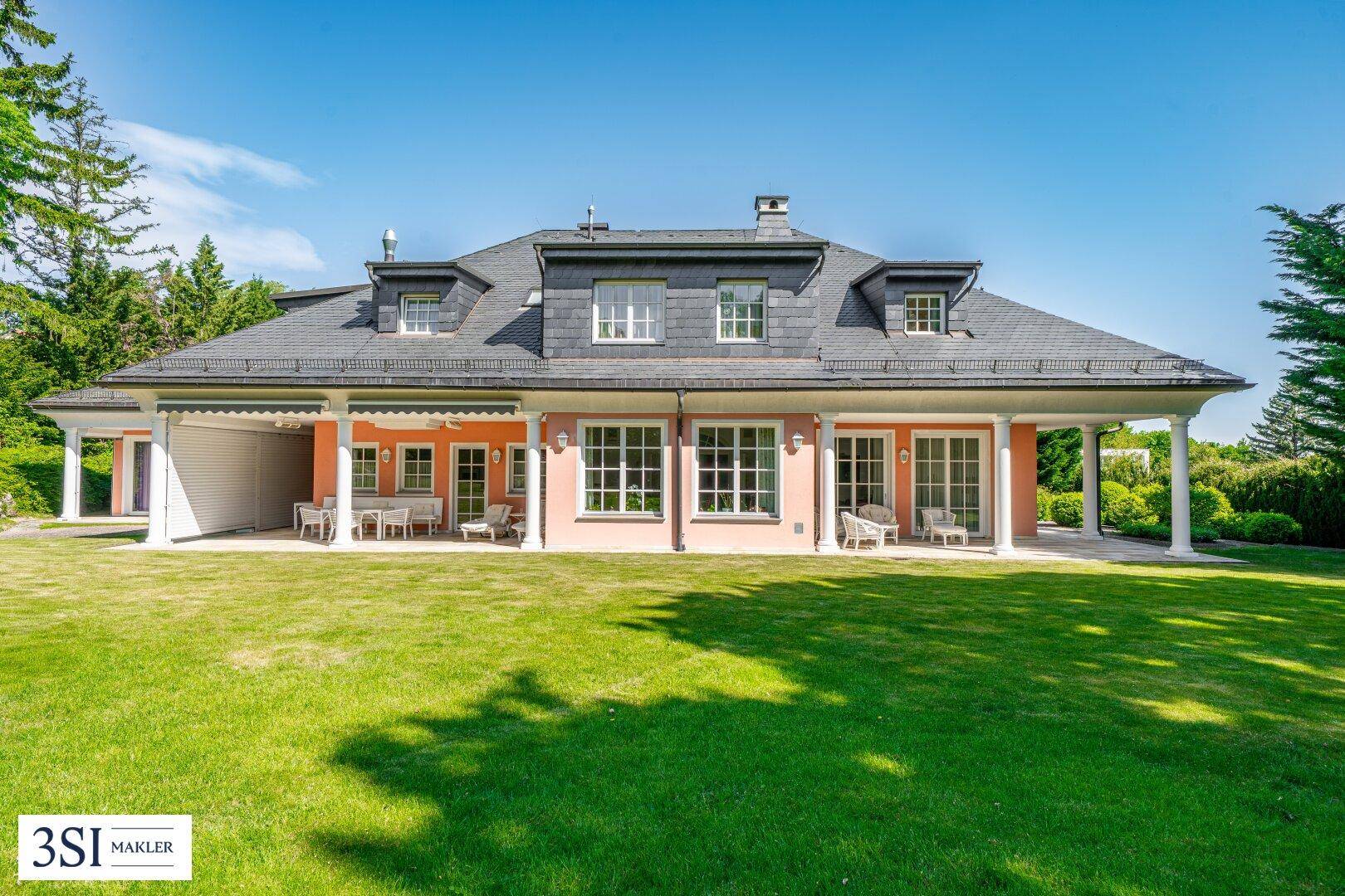Rückansicht der eleganten Villa mit weitläufigem Garten und überdachten Terrassenbereichen.