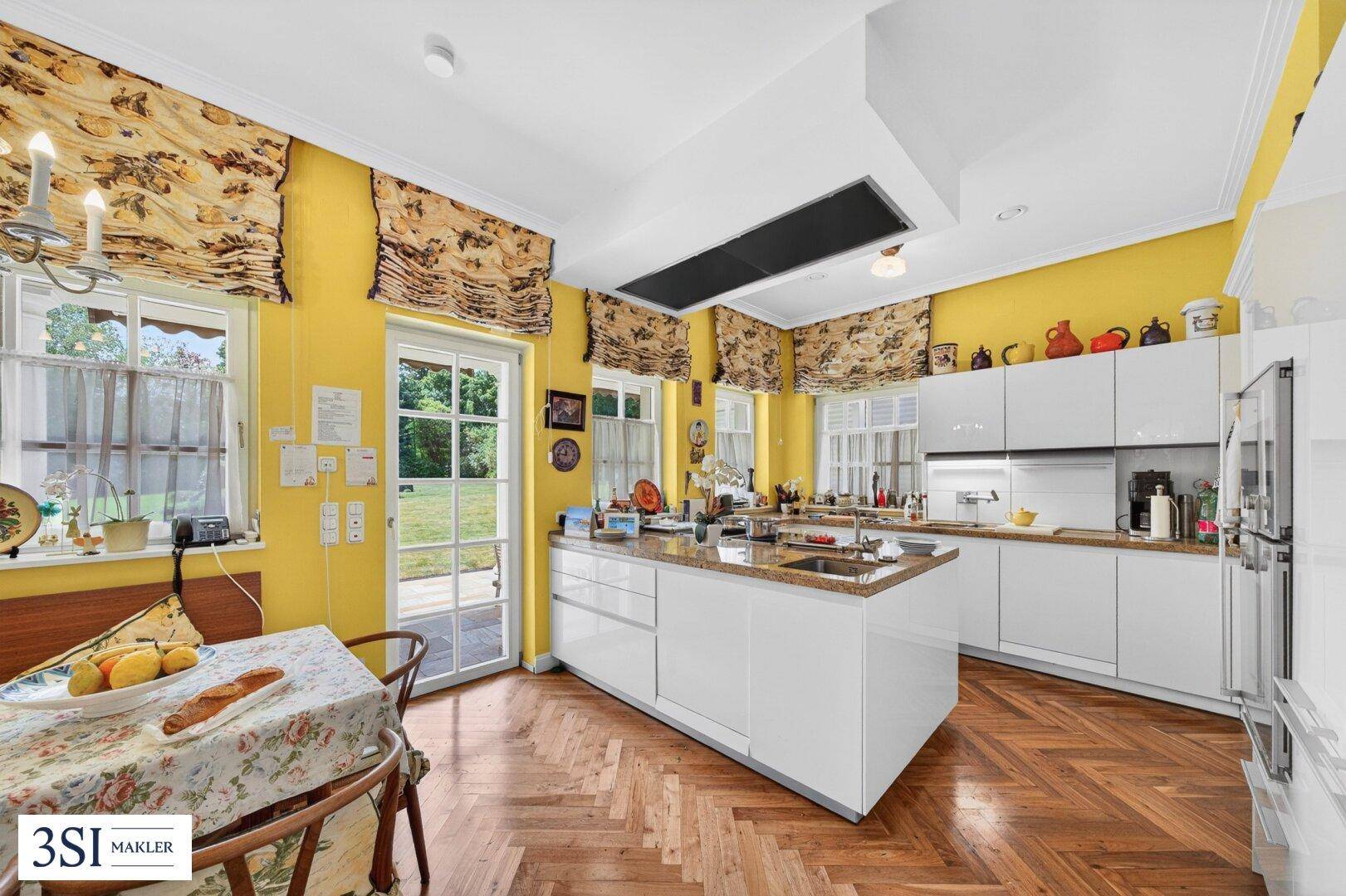 Moderne Küche mit weißen Hochglanzfronten, Kücheninsel und Zugang zum Garten.
