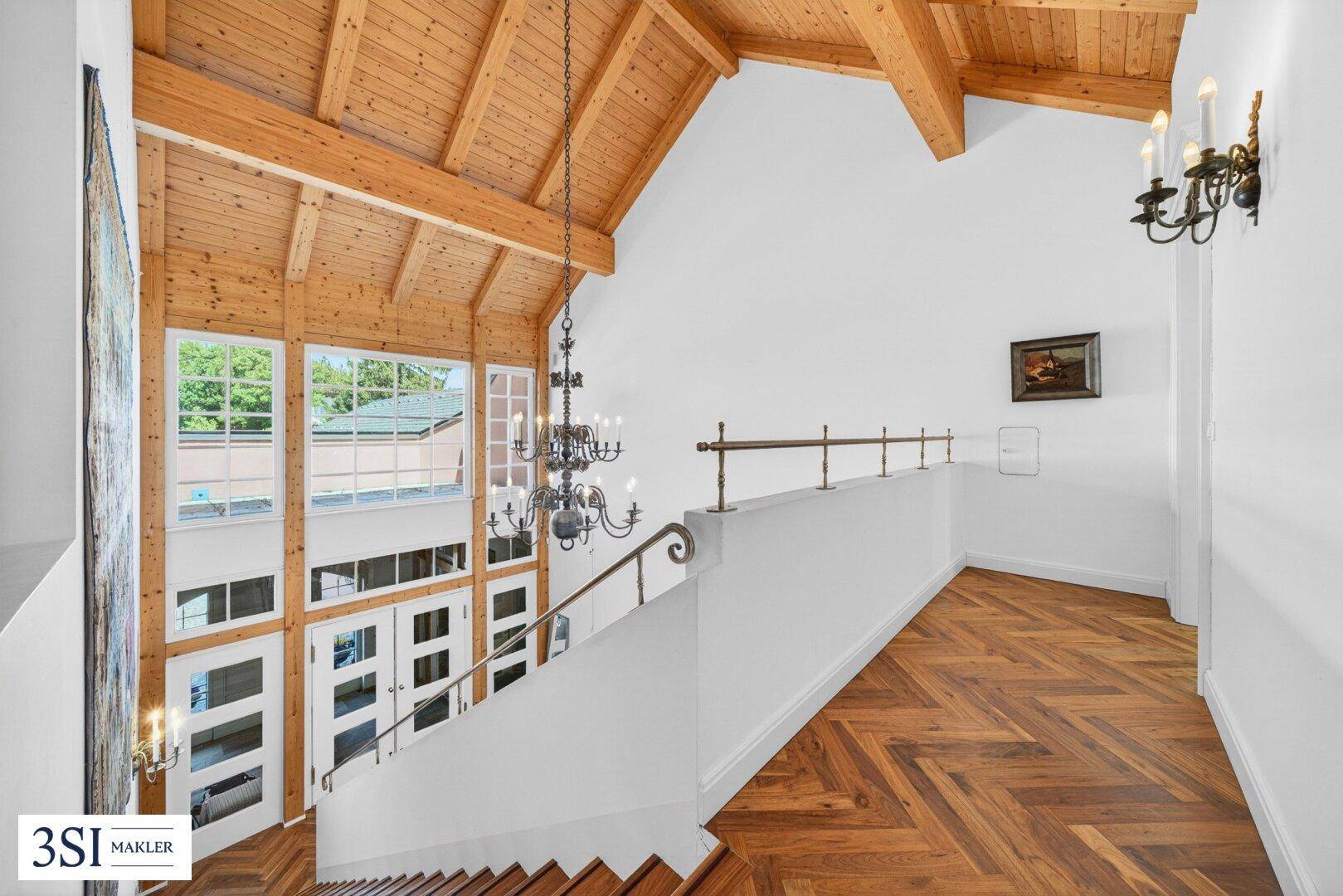 Beeindruckendes Treppenhaus mit hohen Decken, Holzbalken und großen Fenstern.