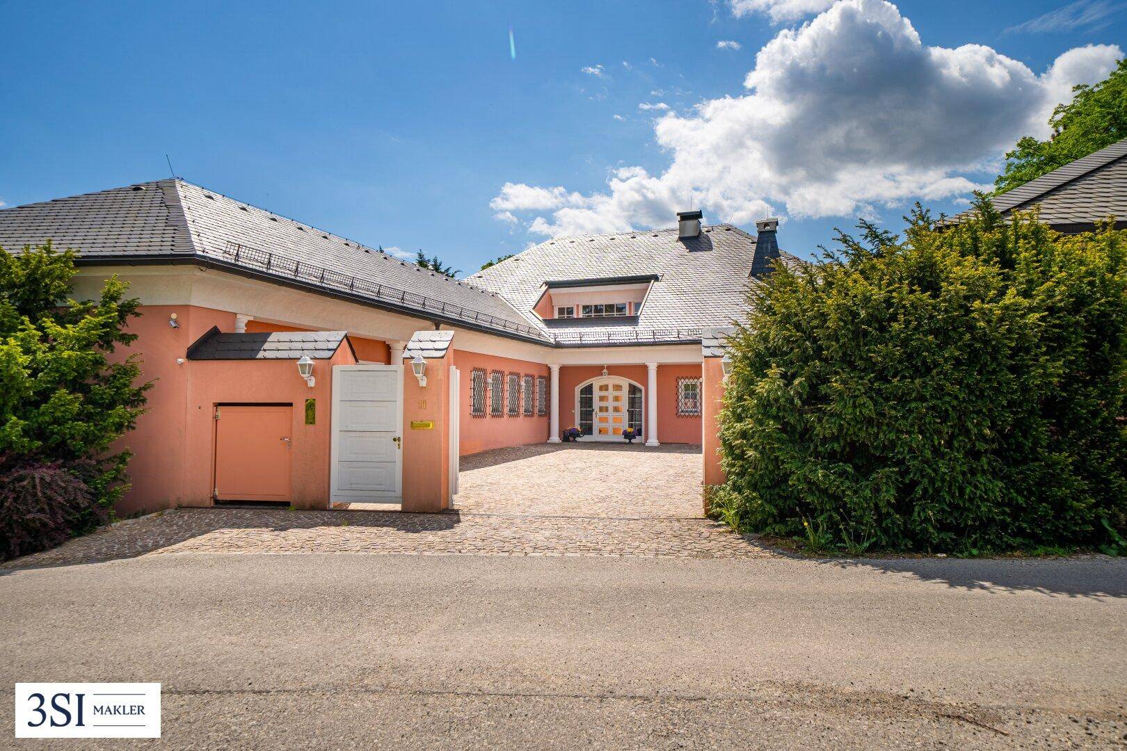 Repräsentativer Eingangsbereich der Villa mit gepflasterter Auffahrt und grüner Hecke.