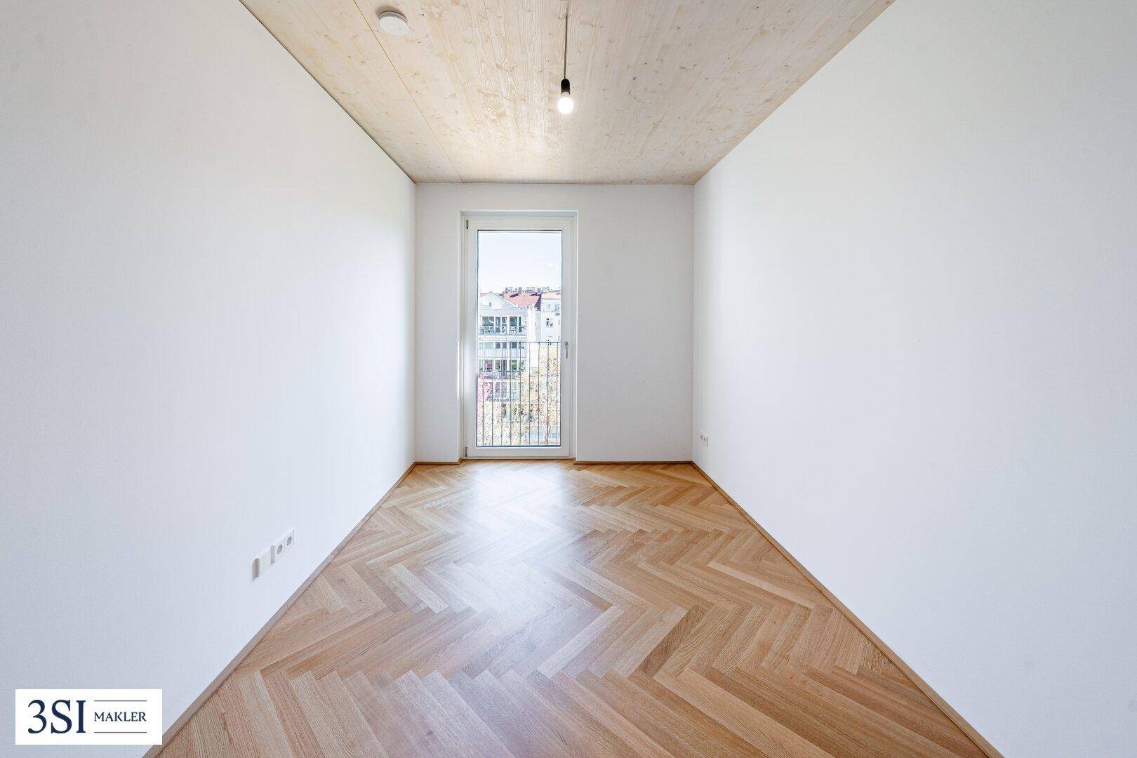 Leerer Raum mit Fischgrätparkett, weißen Wänden und Zugang zu einem Balkon, bereit zur individuellen Gestaltung.