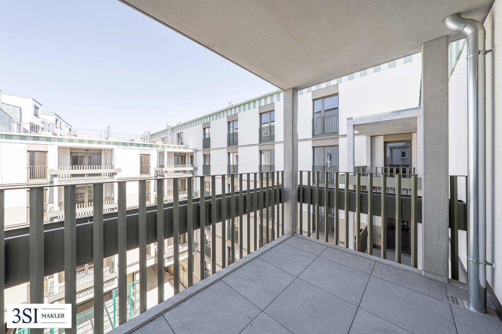 Geräumiger Balkon mit Fliesenboden und Blick auf den Innenhof eines modernen Wohnkomplexes.