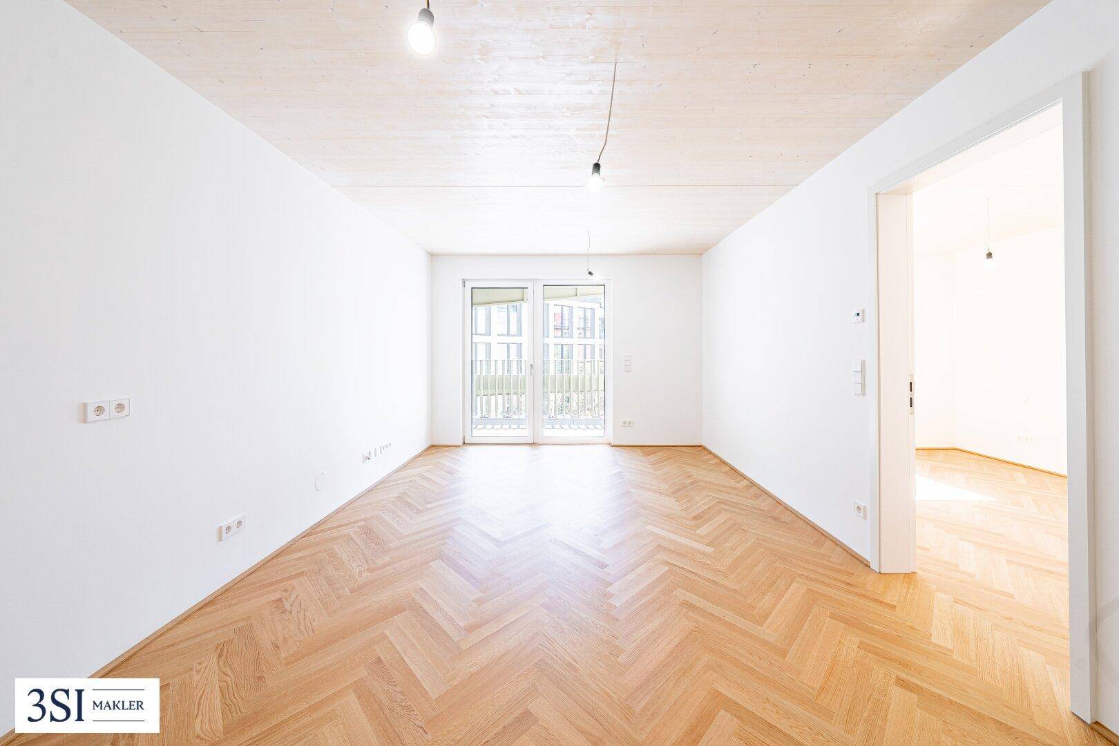 Geräumiges Zimmer mit Fischgrätparkett, Holzbalkendecke und Zugang zu einem Balkon.