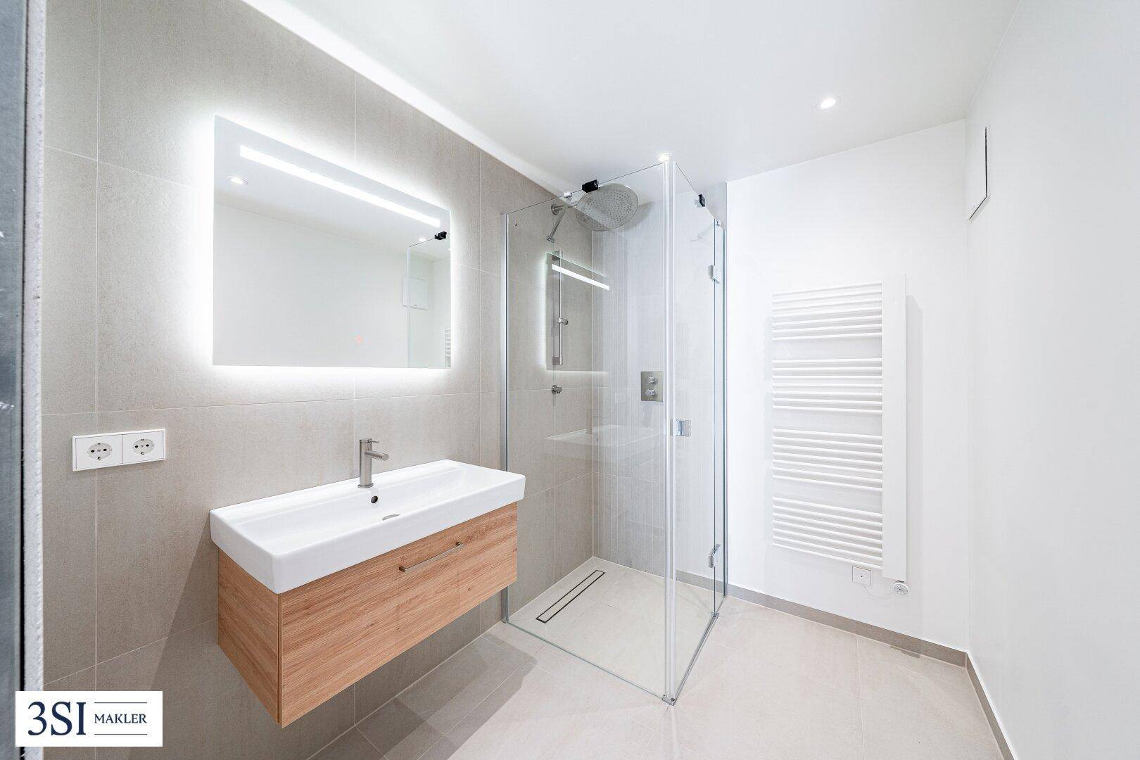 Modernes Badezimmer mit begehbarer Dusche, schwebendem Waschtisch und beleuchtetem Spiegel.