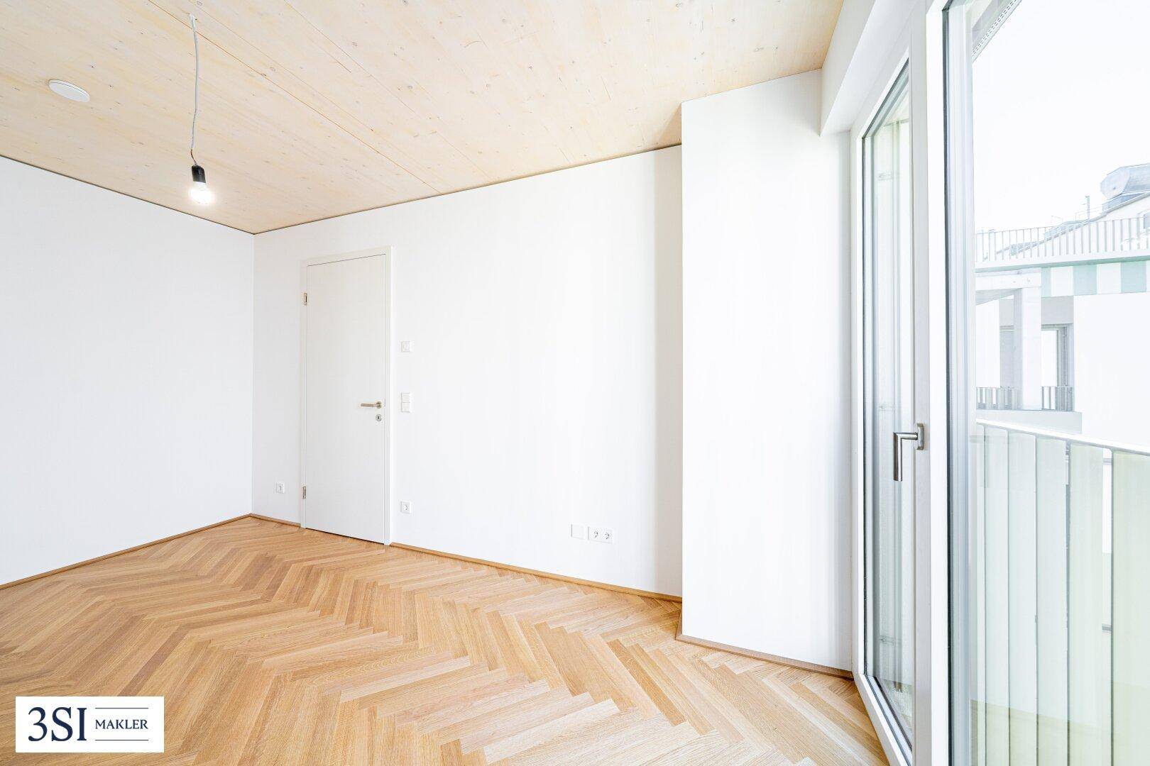 Lichtdurchflutetes Zimmer mit Fischgrätparkett, Holzbalkendecke und Zugang zu einem französischen Balkon.