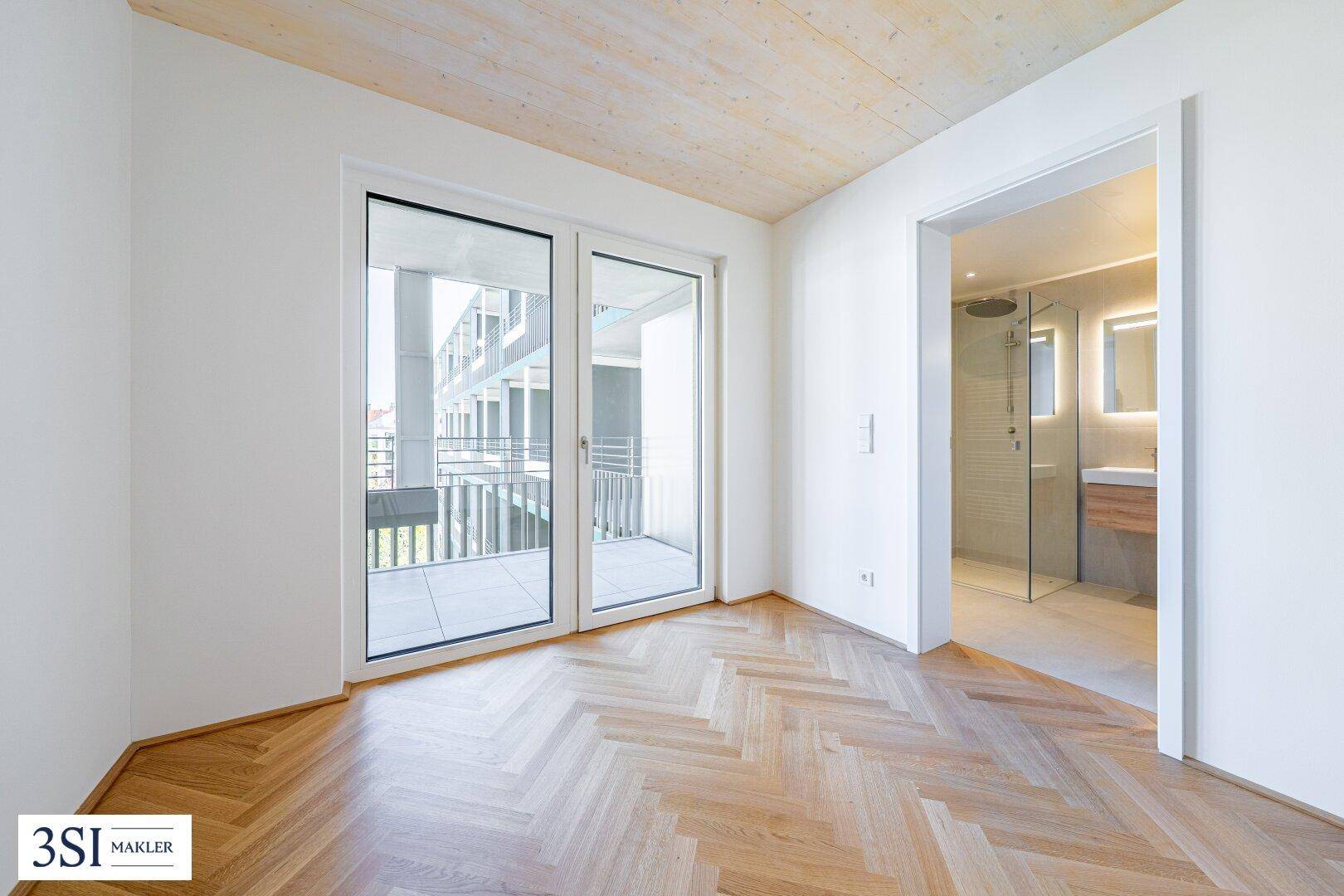 Schlafzimmer mit Fischgrätparkett, Terrassenzugang und direktem Zugang zu einem modernen Badezimmer.