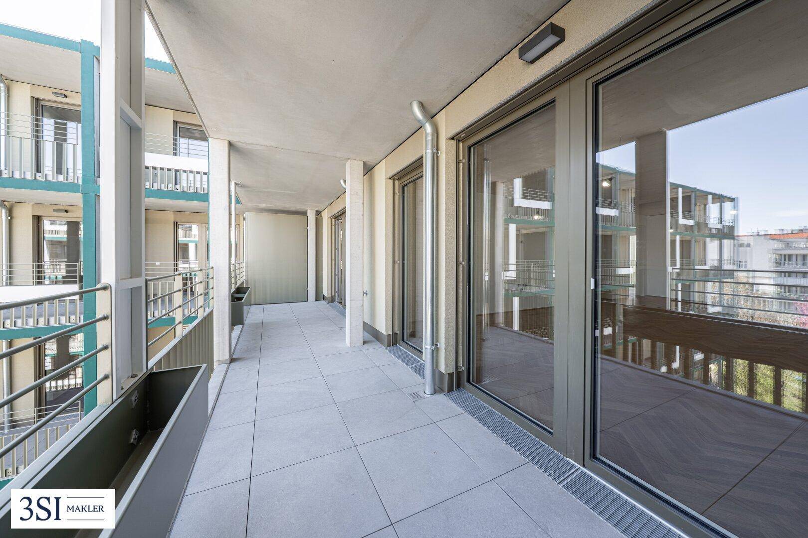 Breite Terrasse mit Fliesenboden und großen Glasfronten, die viel Licht in die Innenräume lassen.