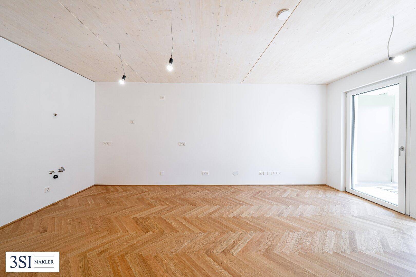 Lichtdurchfluteter Raum mit elegantem Fischgrätparkett und moderner Holzdecke.