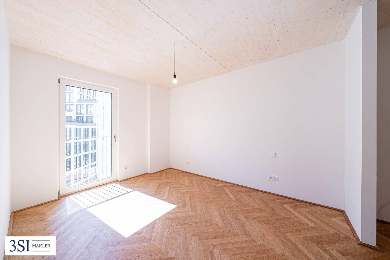 Heller Raum mit Sonnenlicht auf dem Fischgrätparkett und großem Fenster.