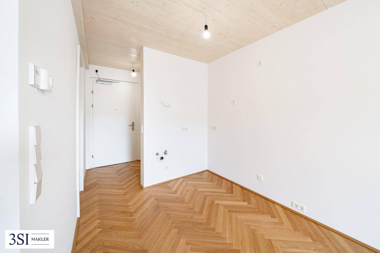 Heller Eingangsbereich mit Fischgrätparkett, Holzdecke und moderner Tür.