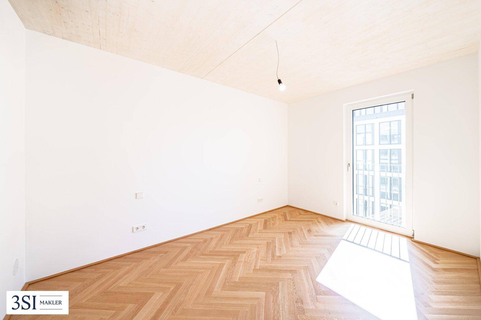 Helles Schlafzimmer mit Fischgrätparkett, Holzbalkendecke und Zugang zu einem französischen Balkon.