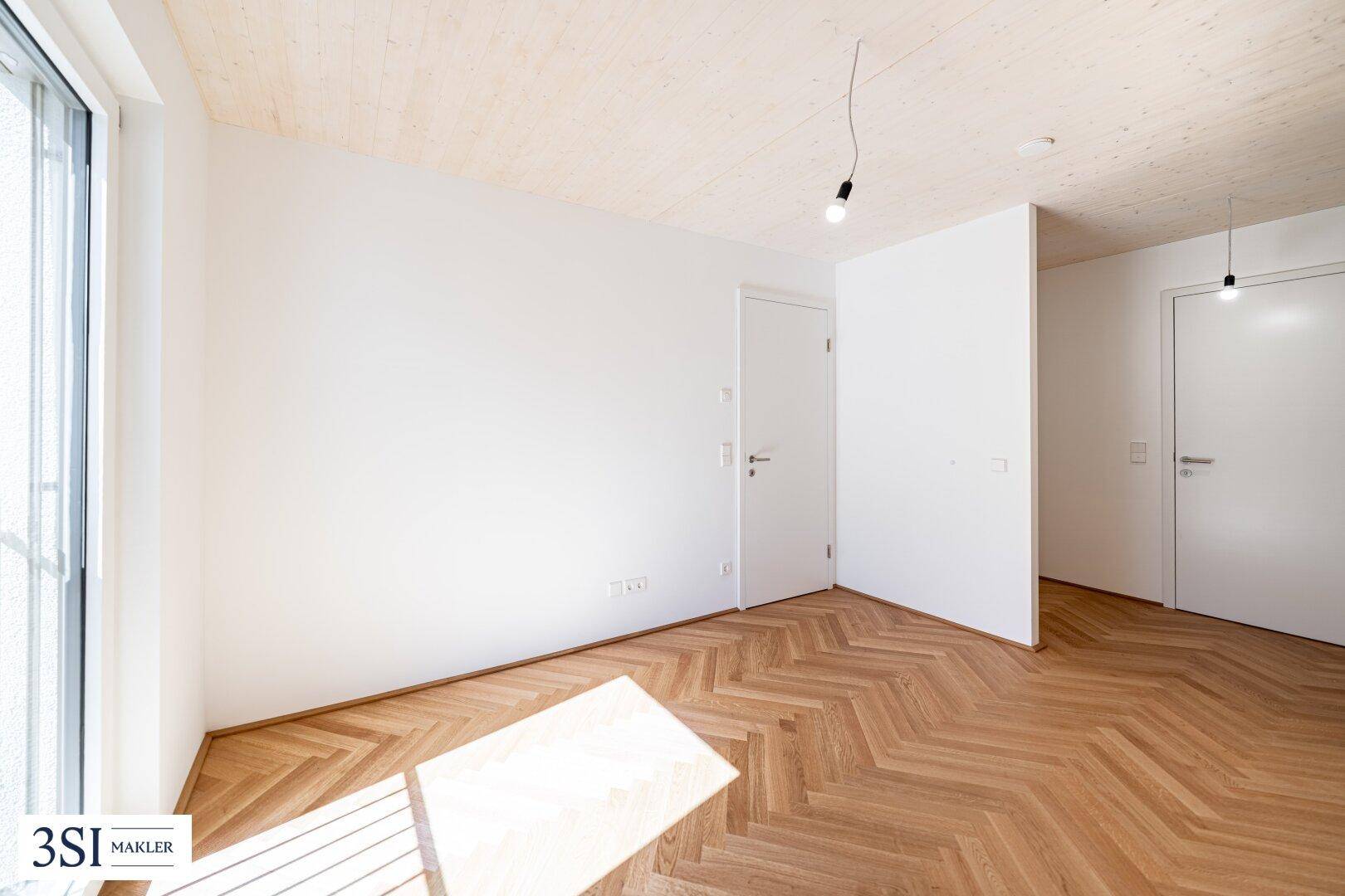 Lichtdurchfluteter Raum mit Fischgrätparkett, Holzbalkendecke und weißen Türen.
