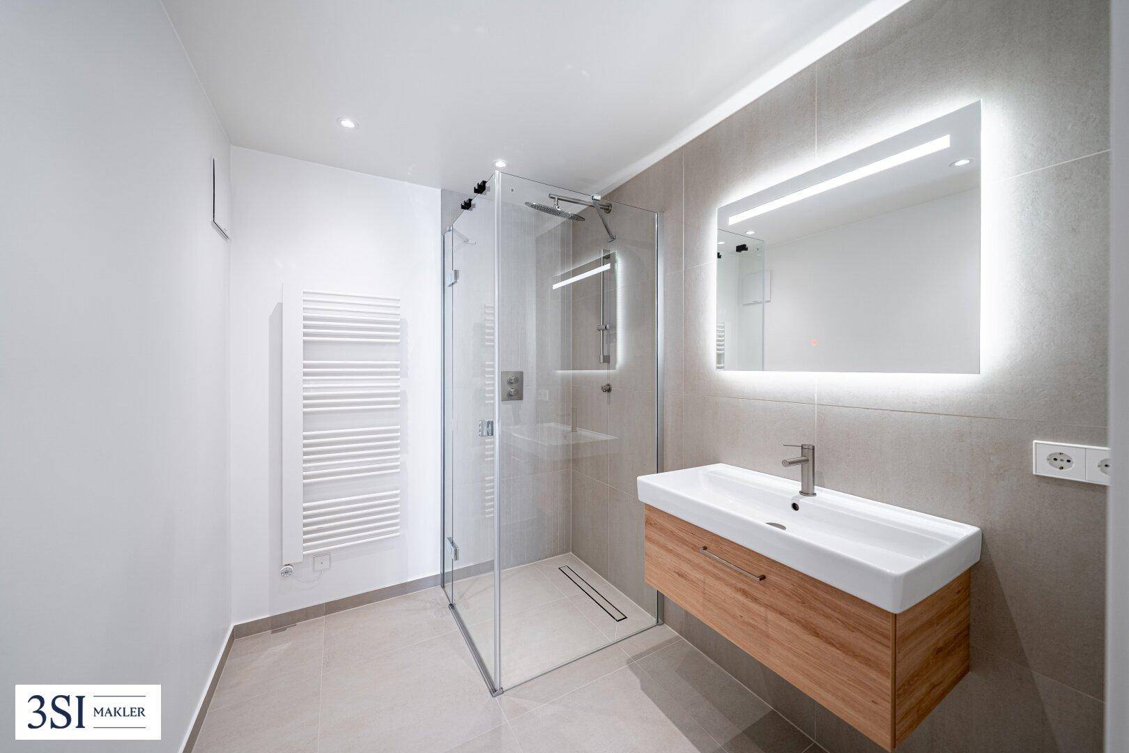 Modernes Badezimmer mit begehbarer Dusche, beleuchtetem Spiegel und Holzwashbasin.