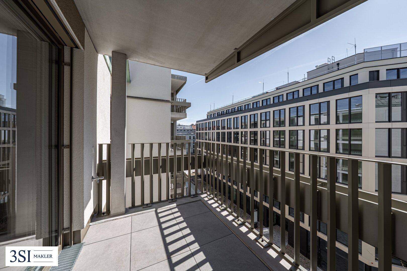 Geräumiger Balkon mit Metallgeländer und Blick auf moderne Stadtgebäude.