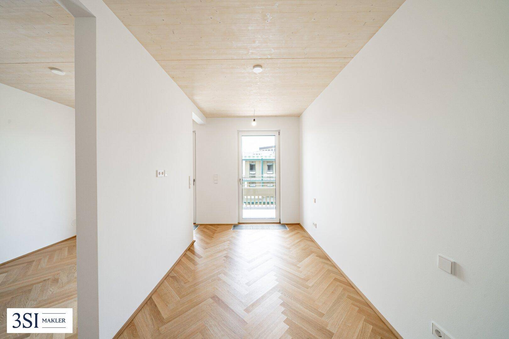 Langer, heller Flur mit Fischgrätparkett und Zugang zu einem französischen Balkon.