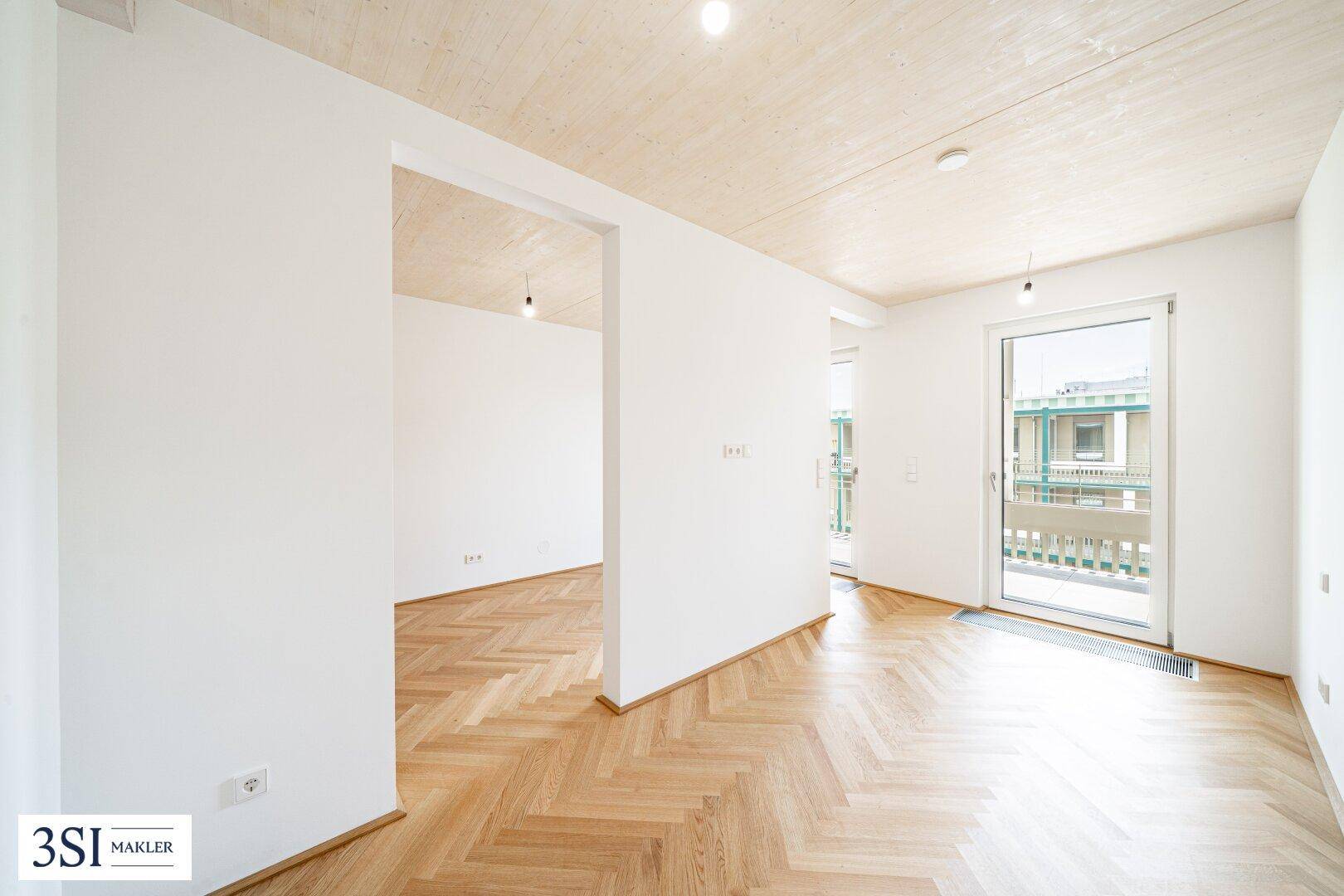 Geräumiger, heller Raum mit Fischgrätparkett, Holzdecke und Zugang zu einem Außenbereich.