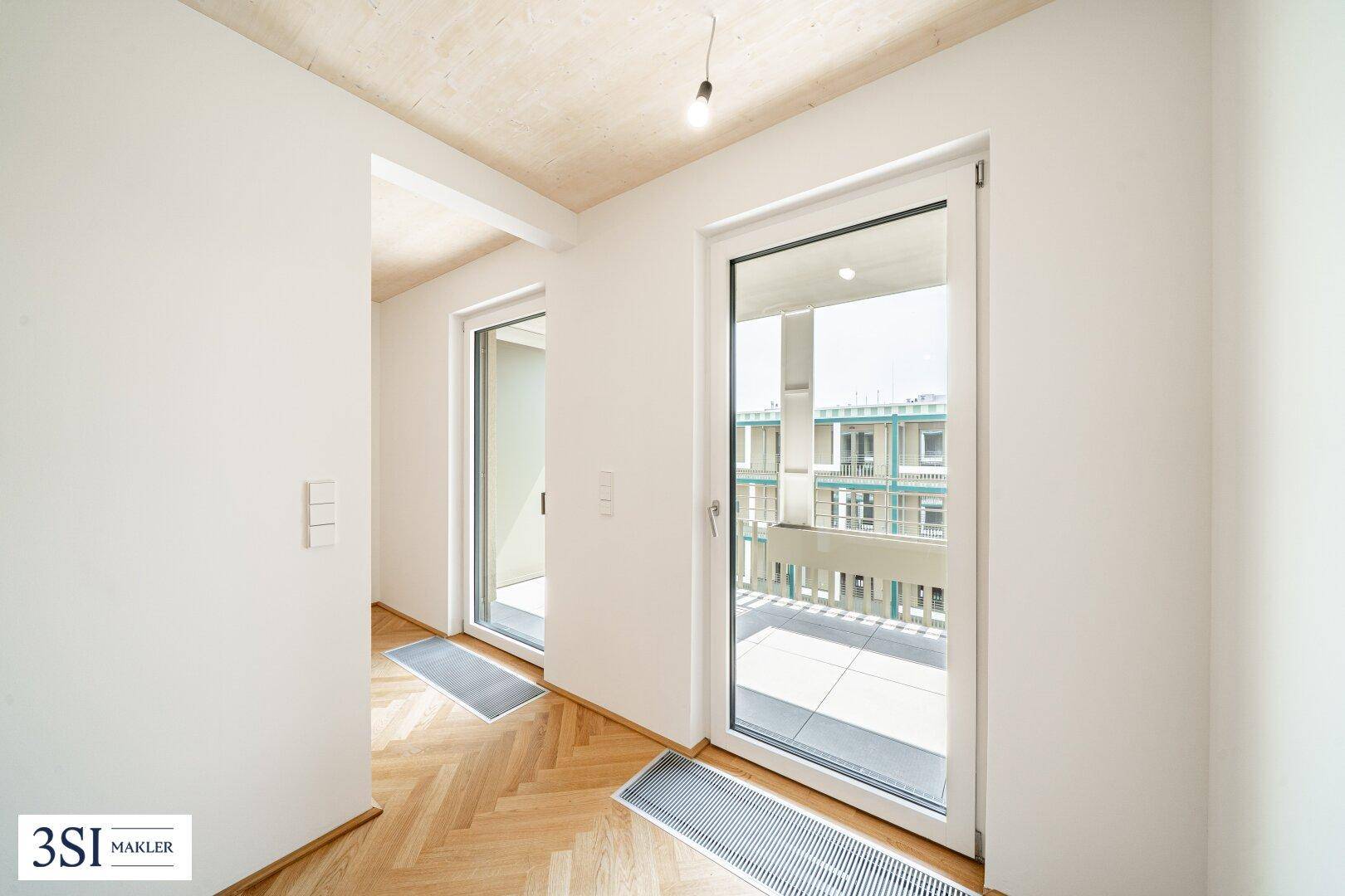 Heller Raum mit Fischgrätparkett und großen Fenstertüren, die viel Tageslicht hereinlassen und Zugang bieten.