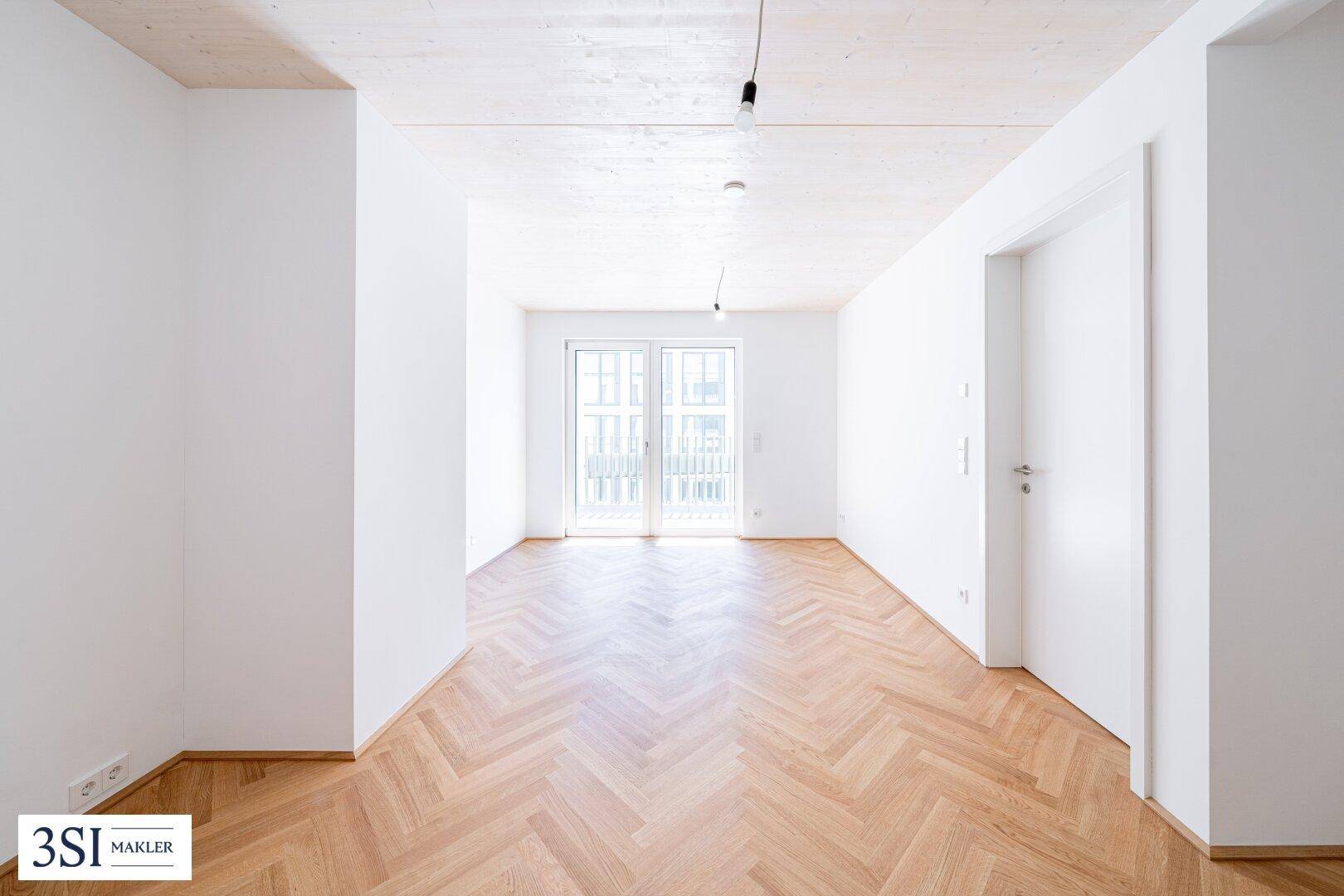 Heller, leerer Raum mit Fischgrätparkett und Zugang zu einem Balkon.