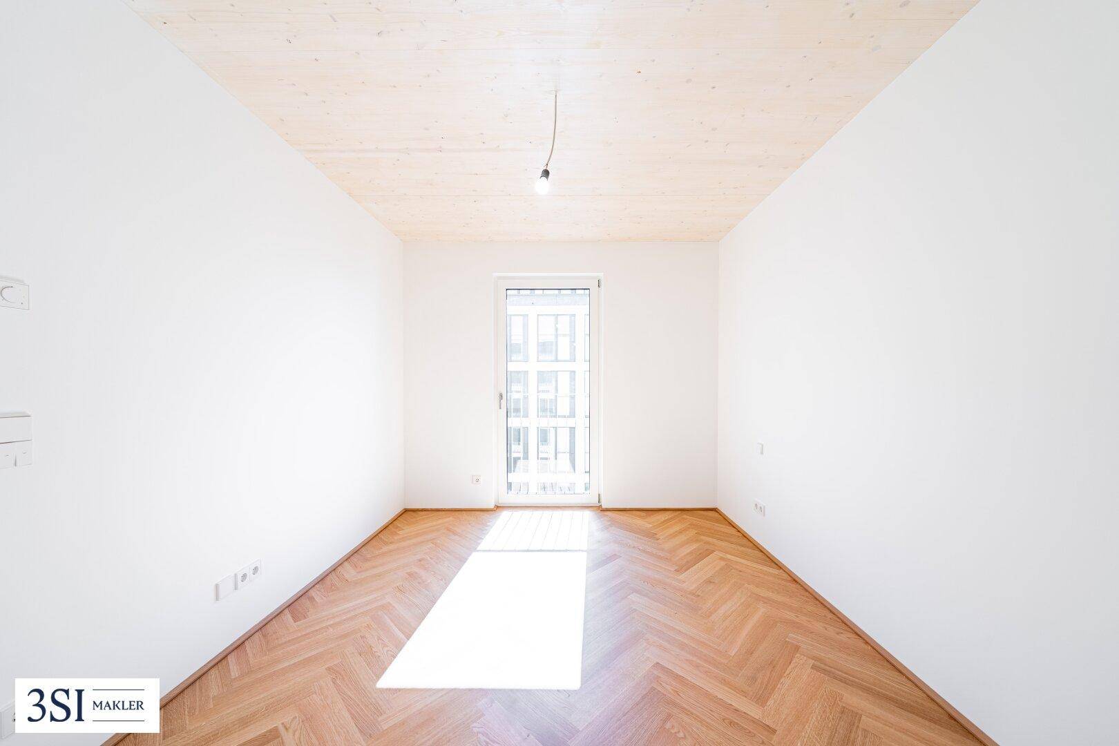 Lichtdurchfluteter Raum mit Fischgrätparkett und Zugang zu einem französischen Balkon.