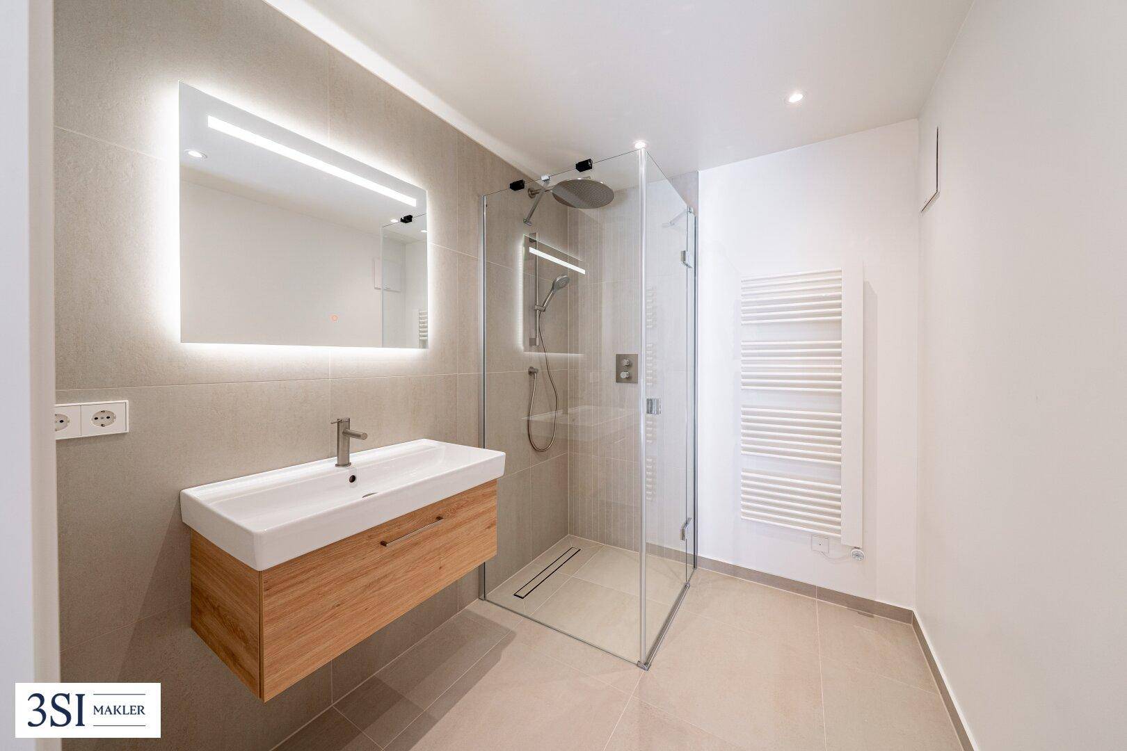 Modernes Badezimmer mit begehbarer Dusche, Waschtisch und beleuchtetem Spiegel.