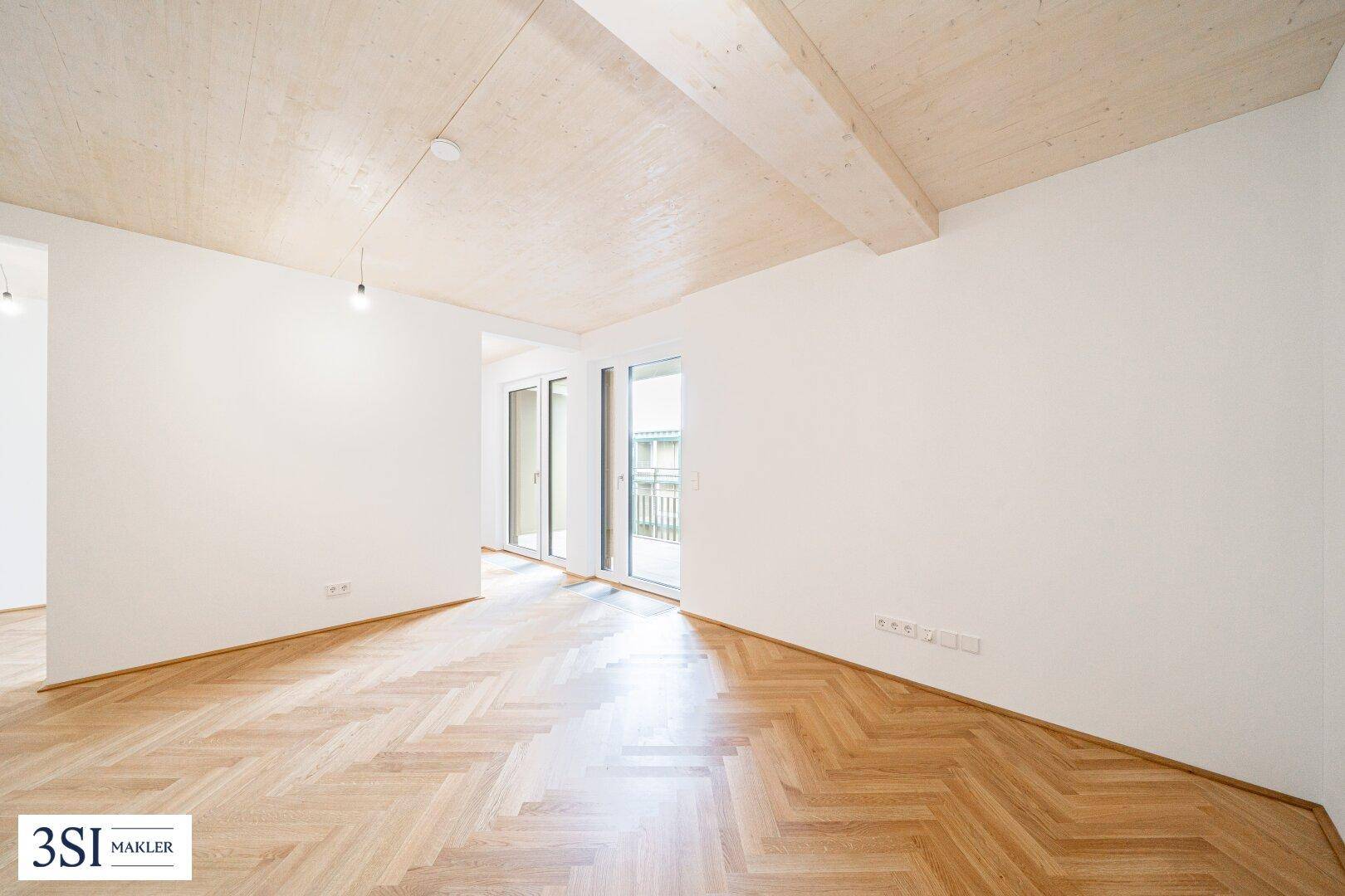 Heller Wohnraum mit Fischgrätparkett, Holzbalkendecke und Zugang zum Außenbereich.