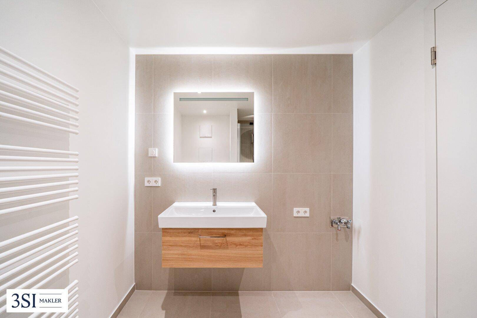 Modernes Badezimmer mit stilvollem Waschtisch, beleuchtetem Spiegel und beheiztem Handtuchhalter.