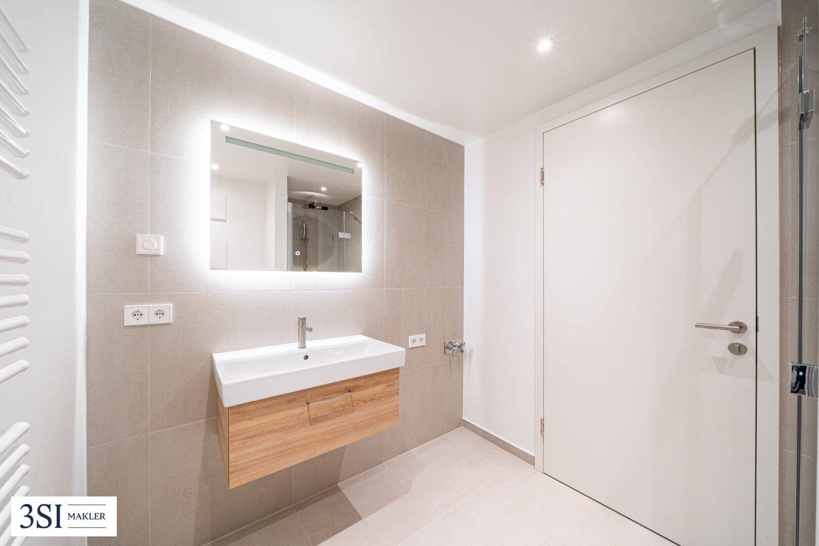 Elegantes Badezimmer mit modernem Waschtisch, beleuchtetem Spiegel und hochwertigen Armaturen.