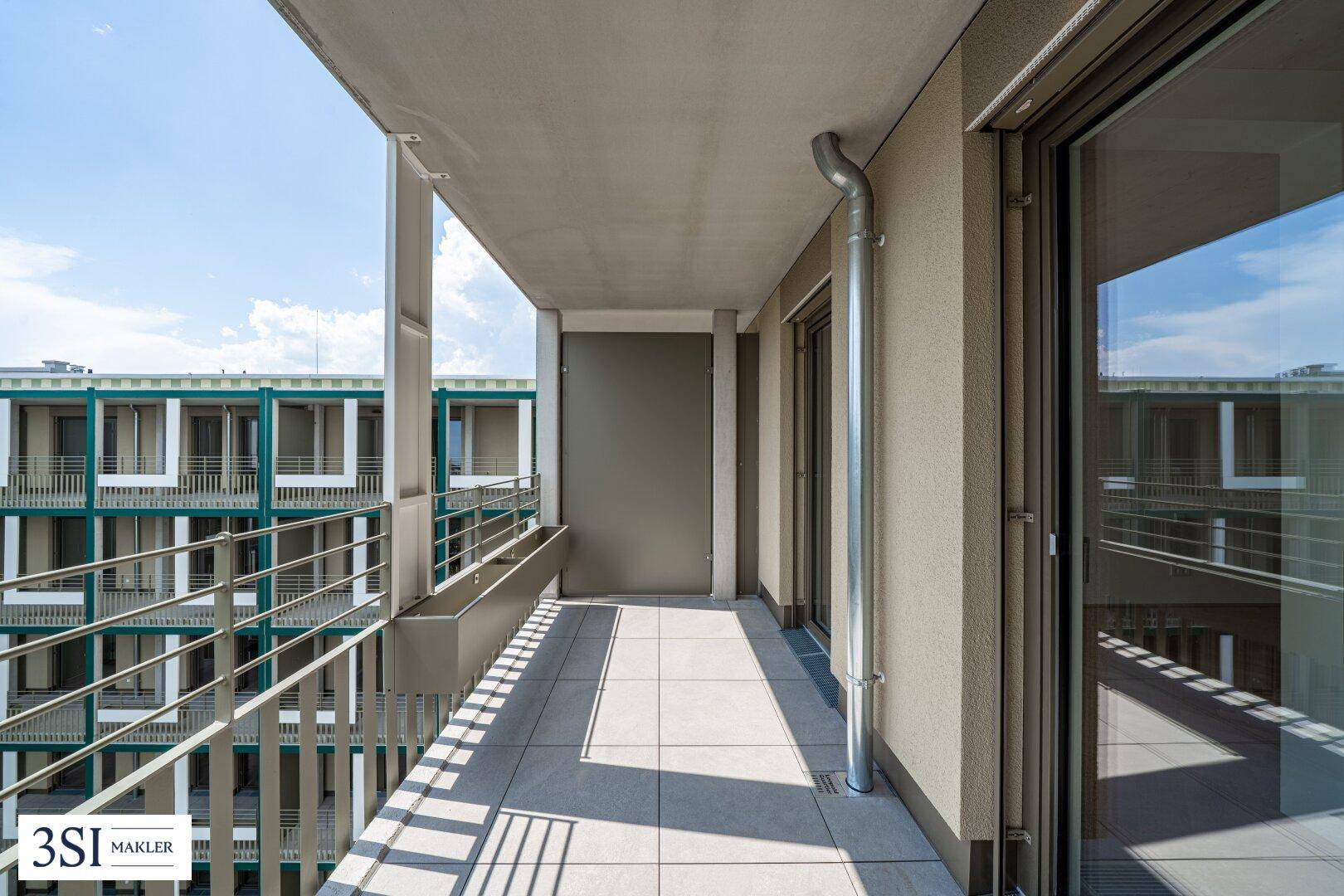 Heller Balkon mit Fliesenboden und moderner Metallbrüstung, umgeben von städtischer Architektur.
