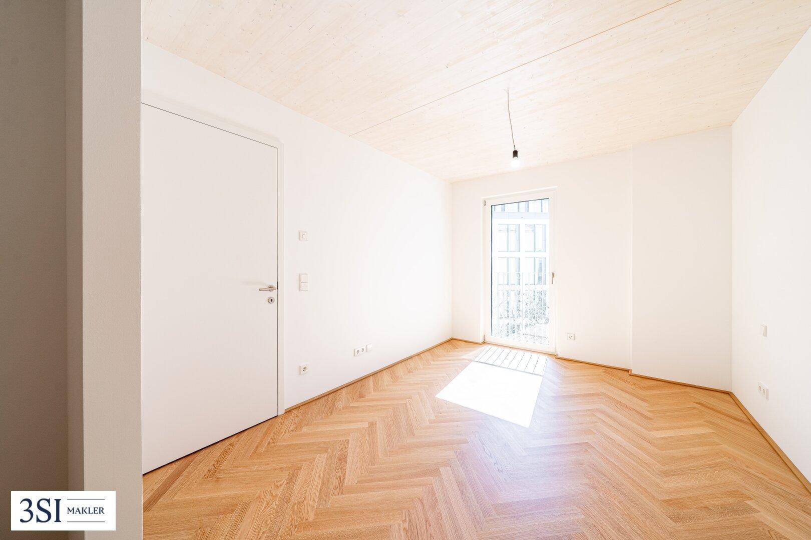 Freundliches Zimmer mit Fischgrätparkett und Balkonzugang, ideal für ein Schlaf- oder Kinderzimmer.