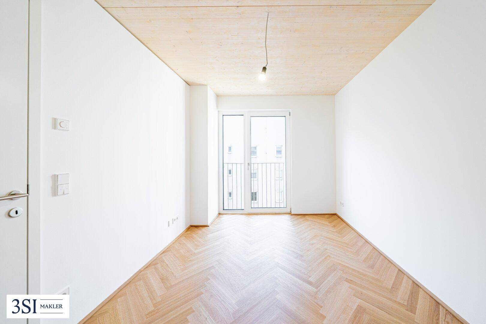 Leeres Schlafzimmer mit Fischgrätparkett und Zugang zu einem französischen Balkon, ideal für Ruhe.