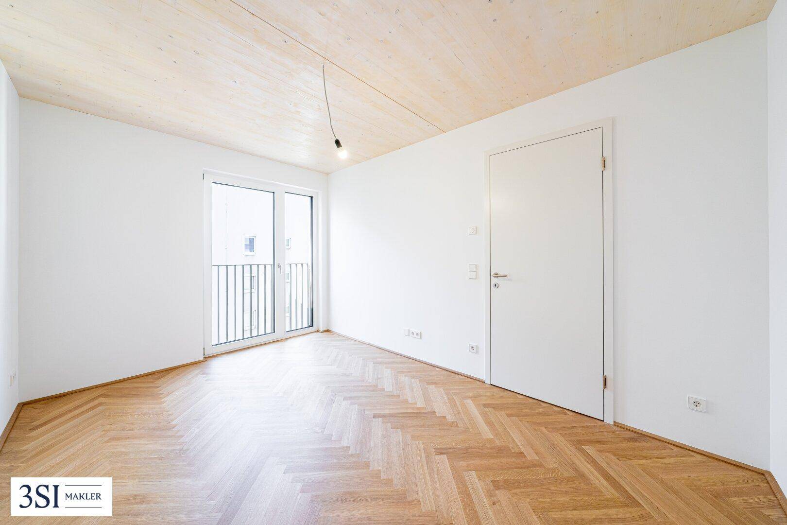 Leeres Schlafzimmer mit Fischgrätparkett und französischem Balkon, bereit zur individuellen Gestaltung.