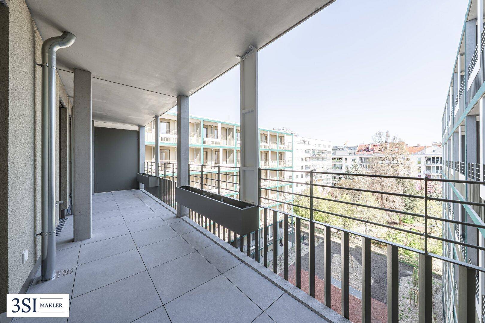 Geräumiger, überdachter Balkon mit Fliesenboden und Blick auf die umliegenden Gebäude.