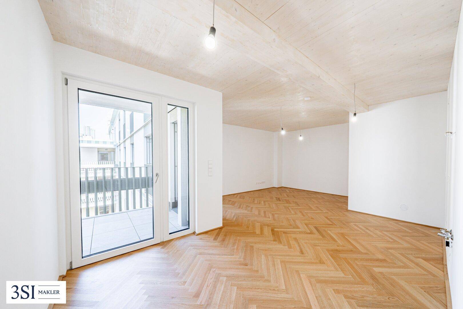Geräumiges, leeres Wohnzimmer mit Fischgrätparkett, hohen Decken und direktem Balkonzugang.