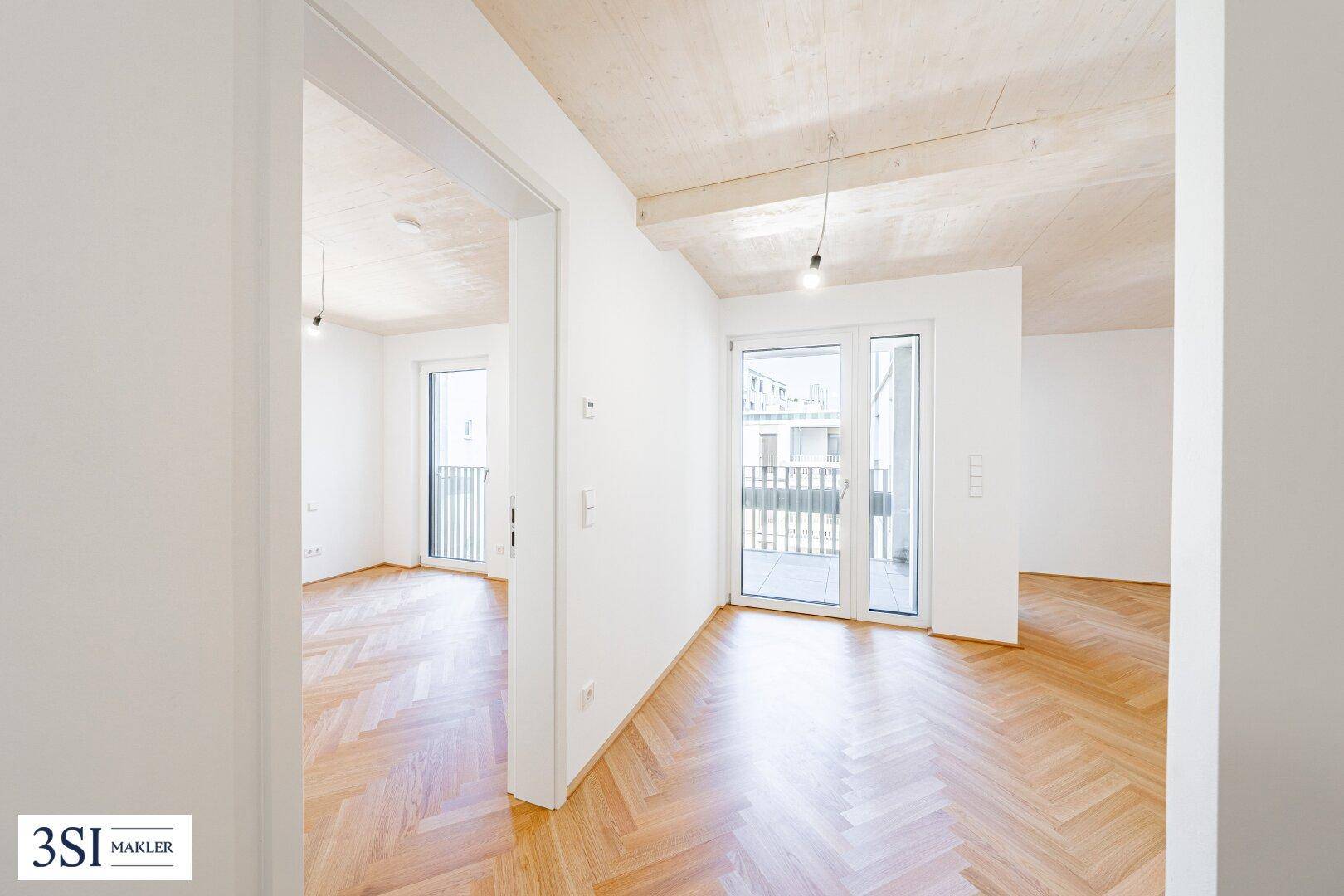 Heller, leerer Raum mit Fischgrätparkett und Zugang zu einem Balkon.